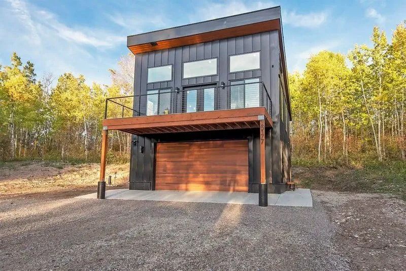 A small house with a garage and a balcony in the middle of a forest.