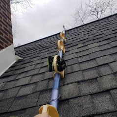 A person is standing on a roof with a ladder attached to it.
