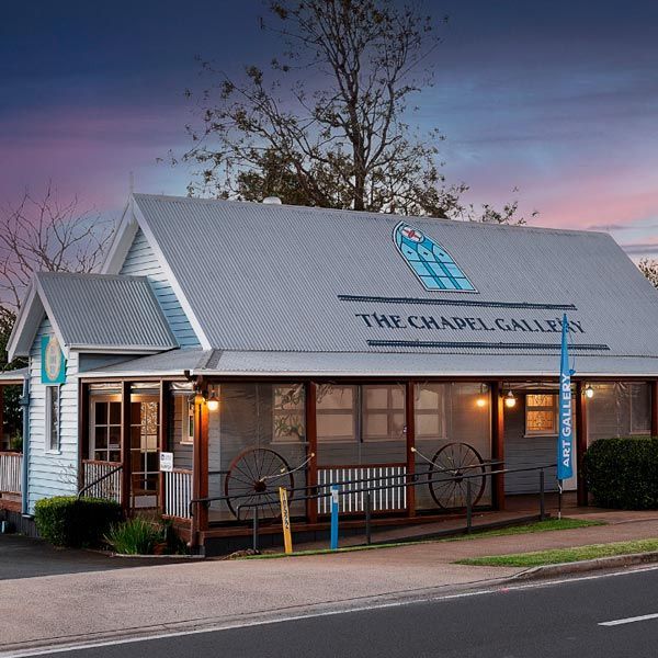 The Chapel Gallery, a white weatherboard building with a grey roof, set against a sunset sky.