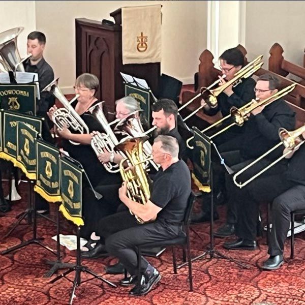 A brass band performs in a church, with musicians playing tubas, trombones, and euphoniums while seated in rows.