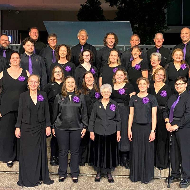 Formal choir group posing on steps, dressed in black with purple accents.