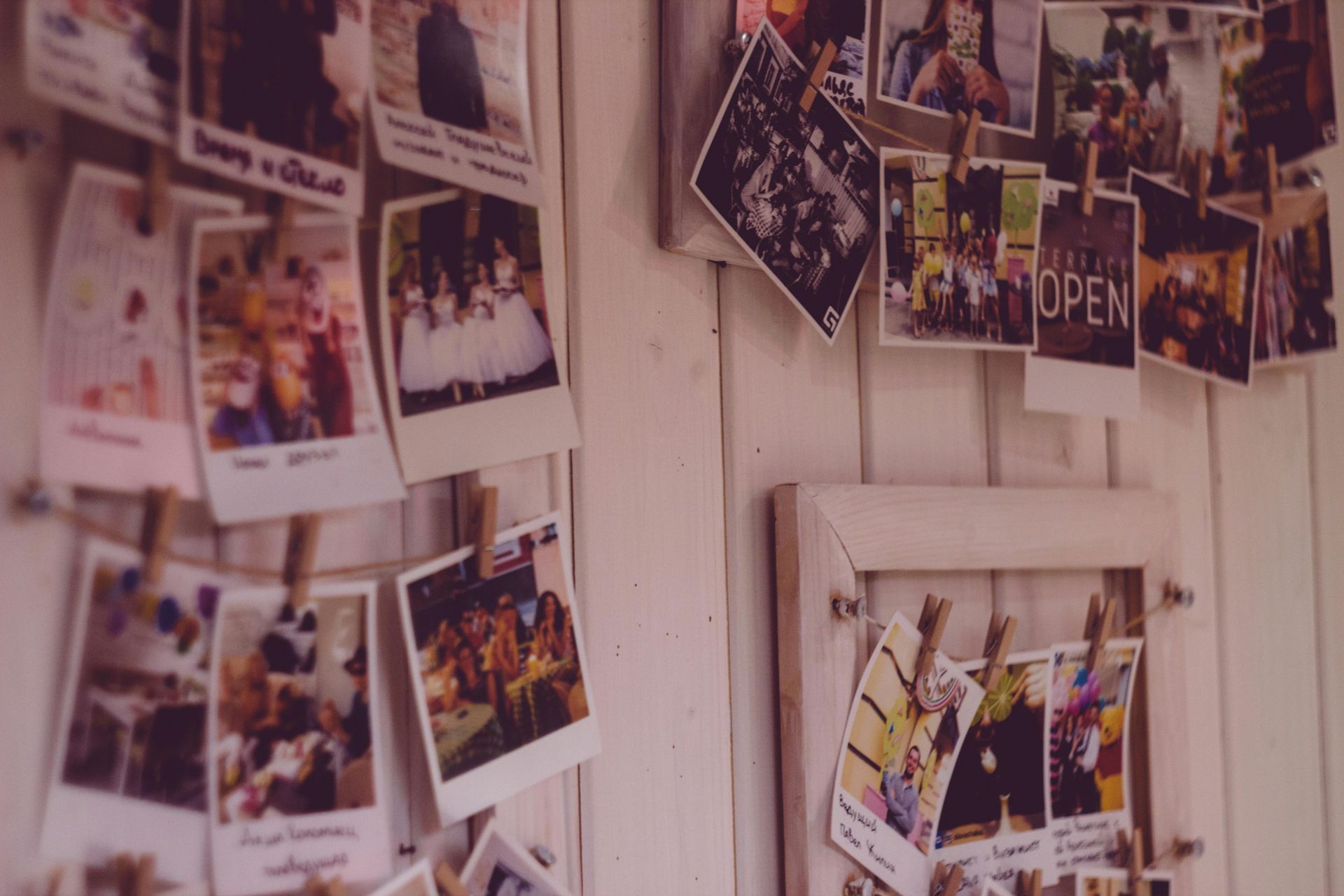 Polaroid photos hanging on a white wall, displaying various memories; some in frames, others pinned with small clips.