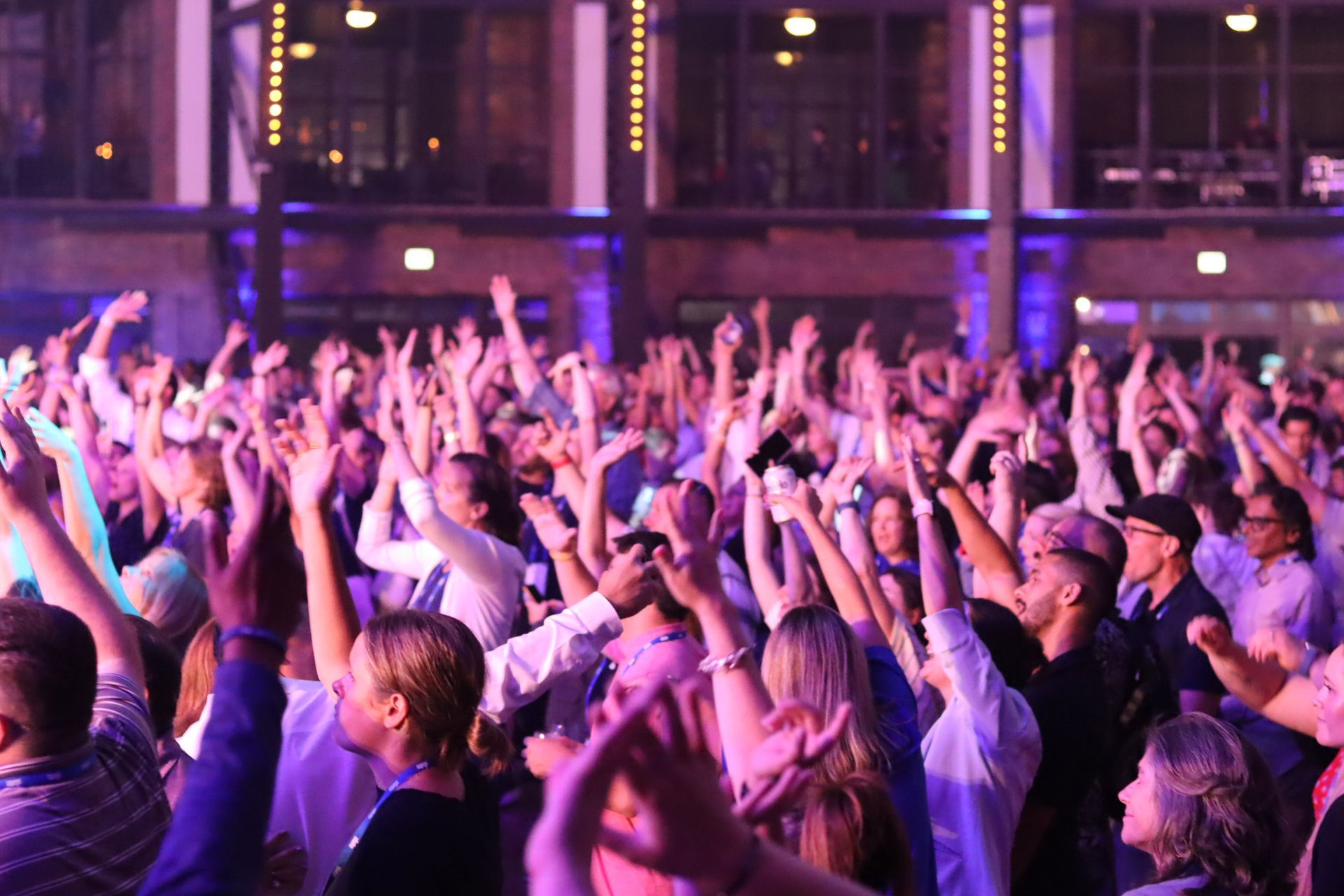 A crowd of people in a brightly lit indoor venue cheers with arms raised during a lively event.