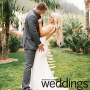 A bride and groom in wedding attire embrace affectionately on a stone garden path.