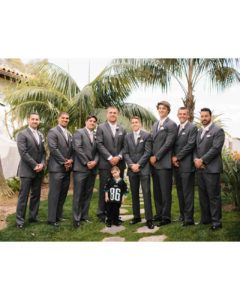 A group of men in grey suits standing outdoors in a garden, with a young child in a sports jersey standing in the center.