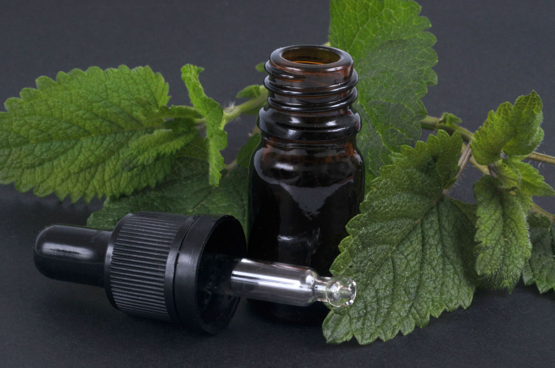 Un flacon d'huile essentielle à côté d'un compte-gouttes et de feuilles de menthe.