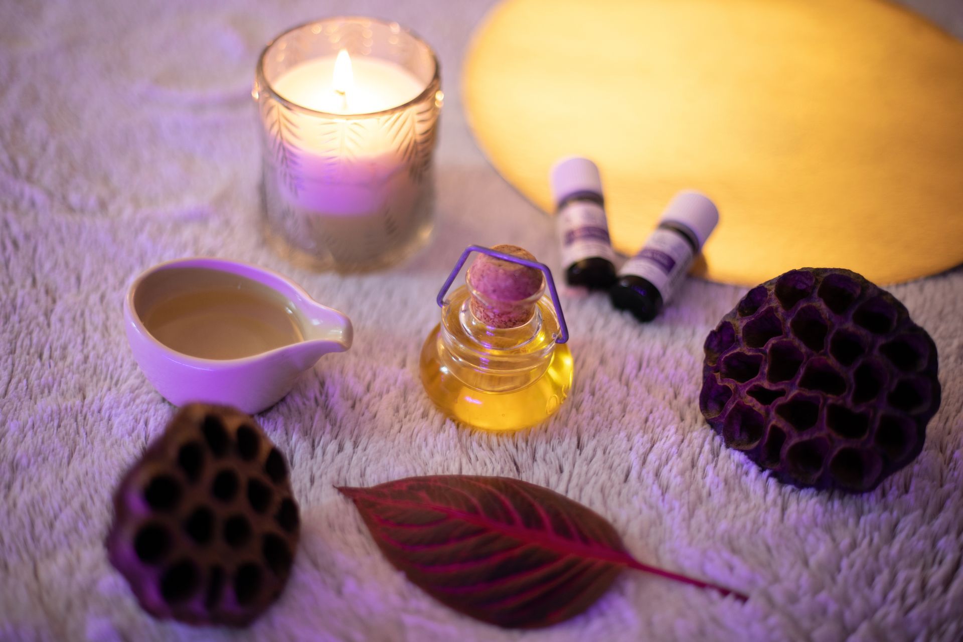 Une bougie, une bouteille d'huile, un bol d'huile et une feuille sont sur une table.