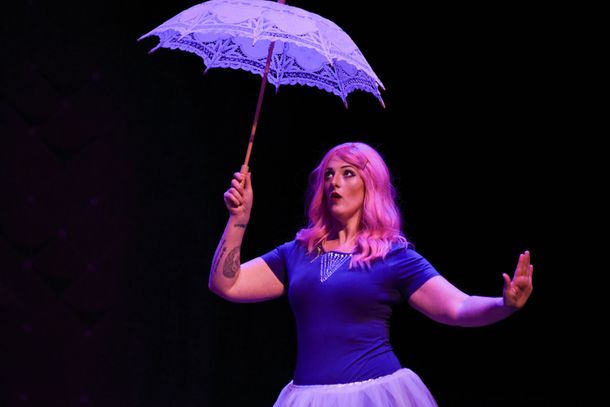 Woman with pink hair holds a white parasol, looking up with surprise against a dark background.