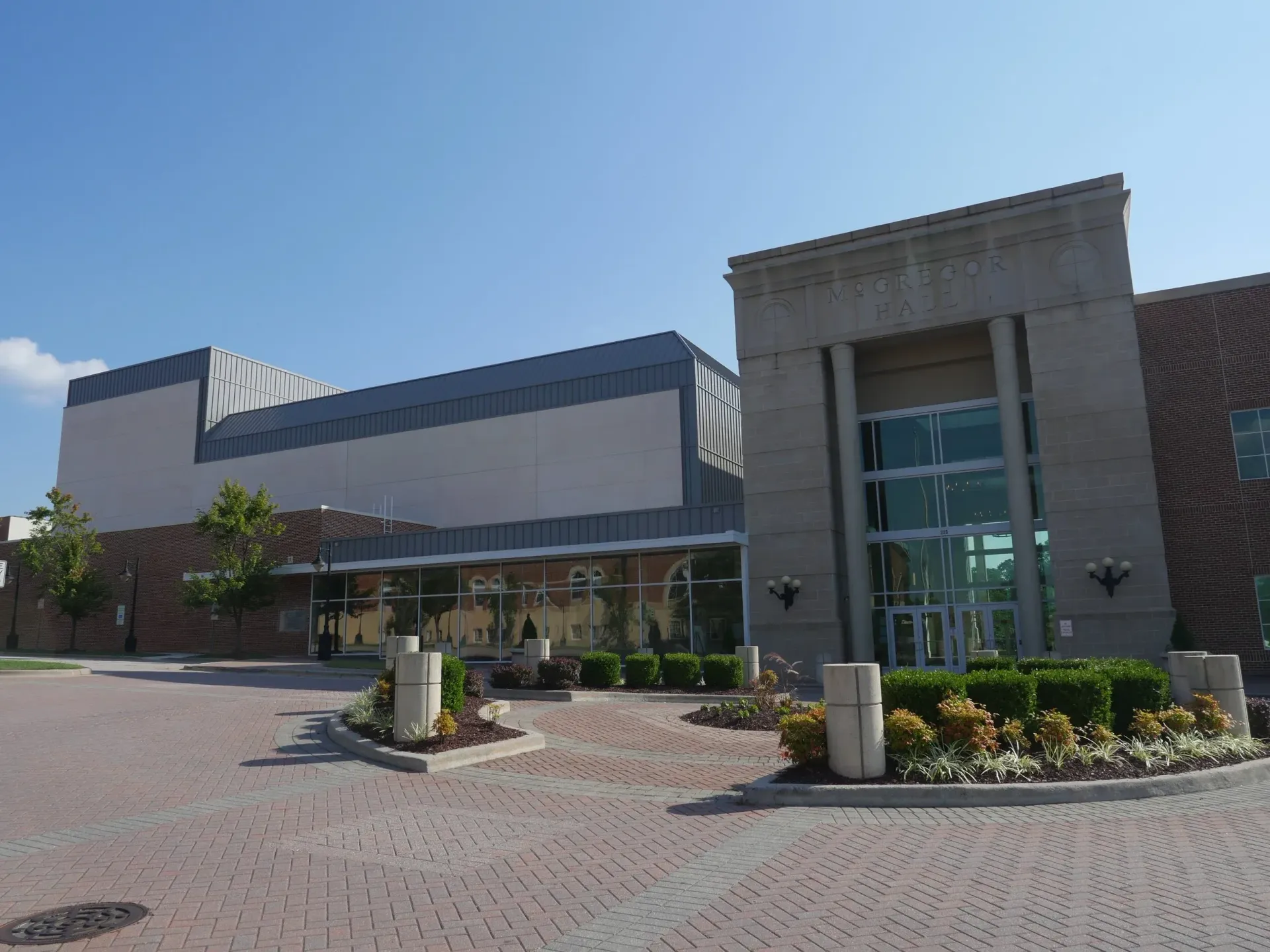 Modern brick and concrete building with glass entrance and landscaped garden on a sunny day.