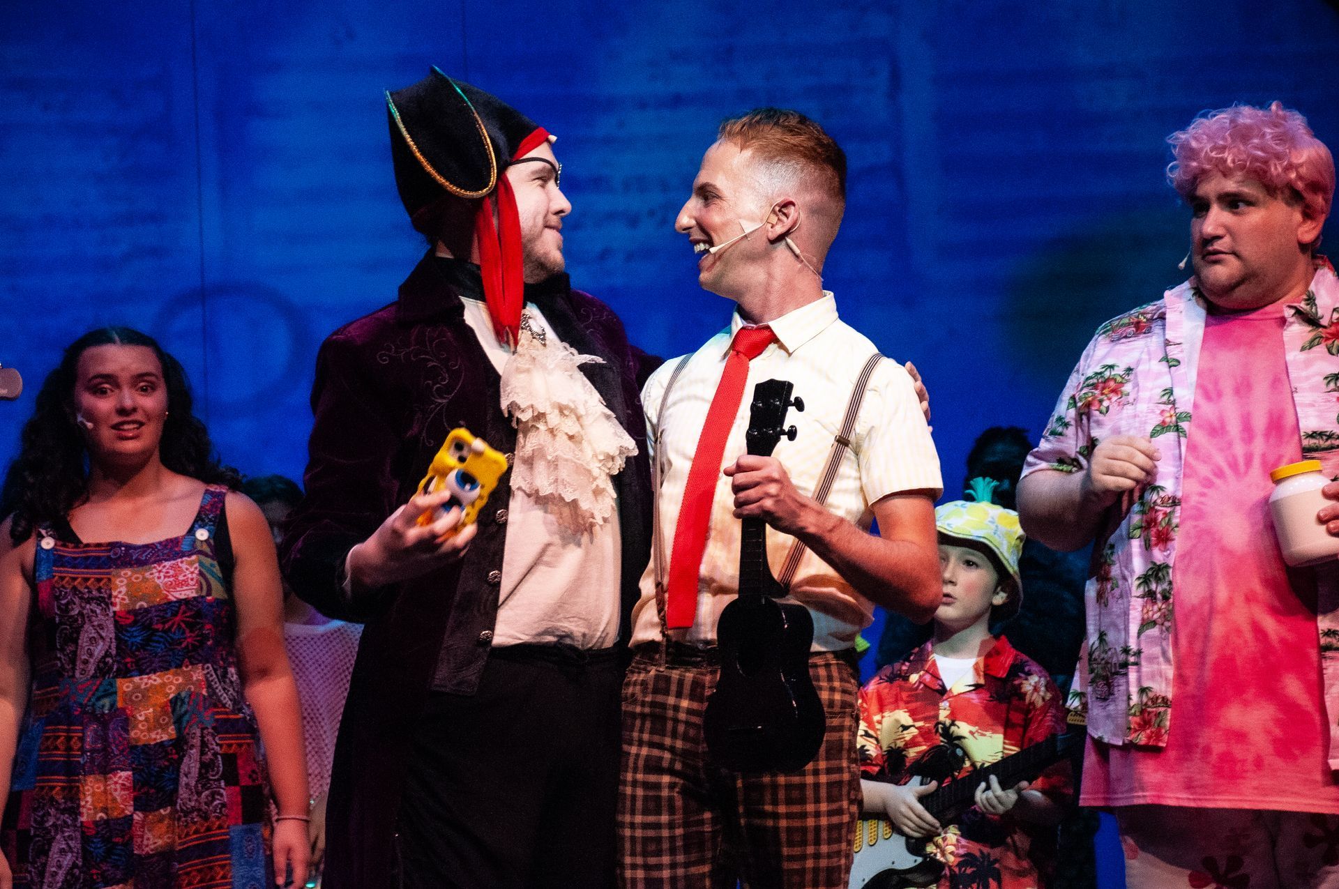 Stage production of SpongeBob characters: pirate, SpongeBob, other characters, all smiling. Bright colors, stage setting.