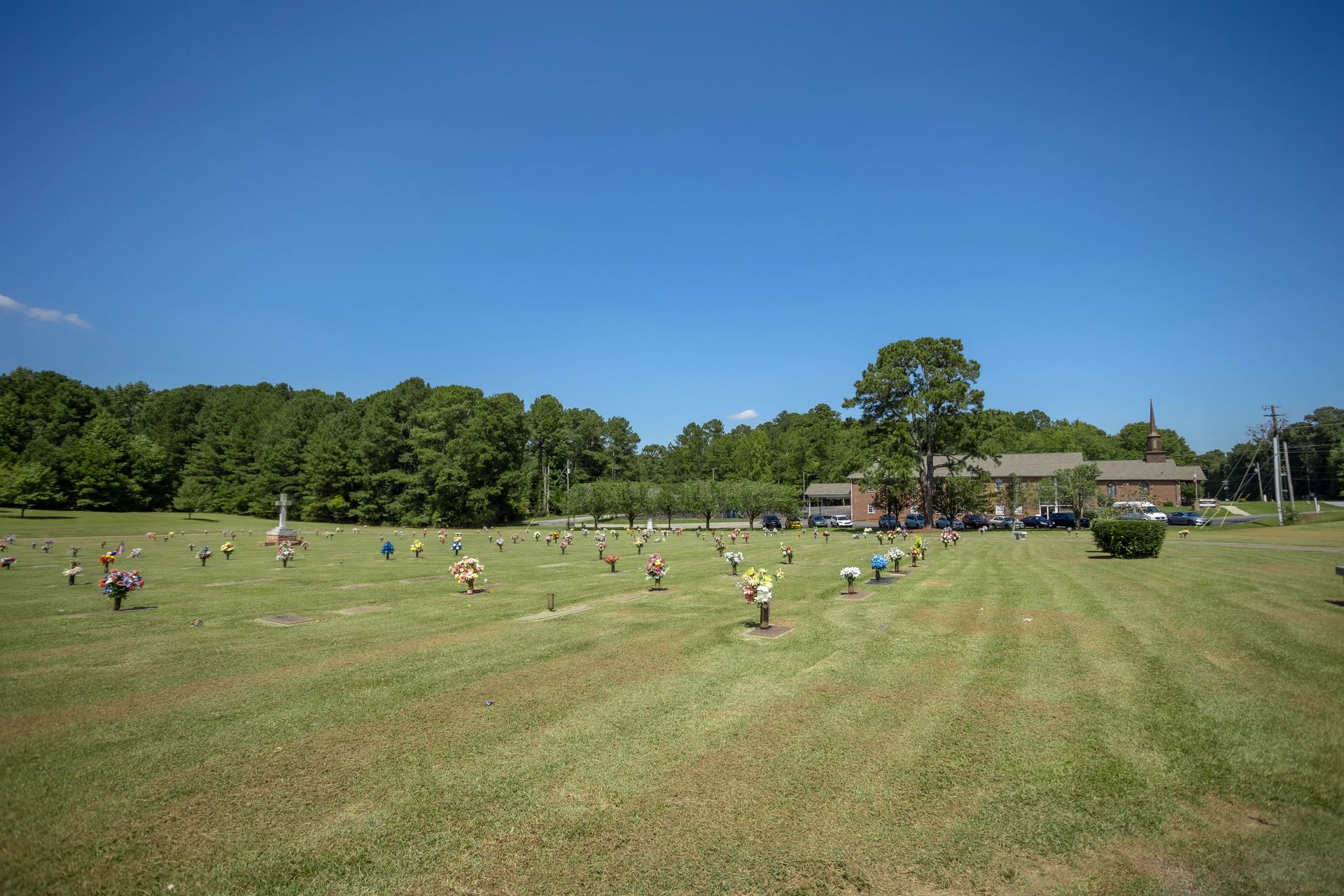 A cemetery with grave markers scattered across a grassy lawn, with trees and a building in the background.