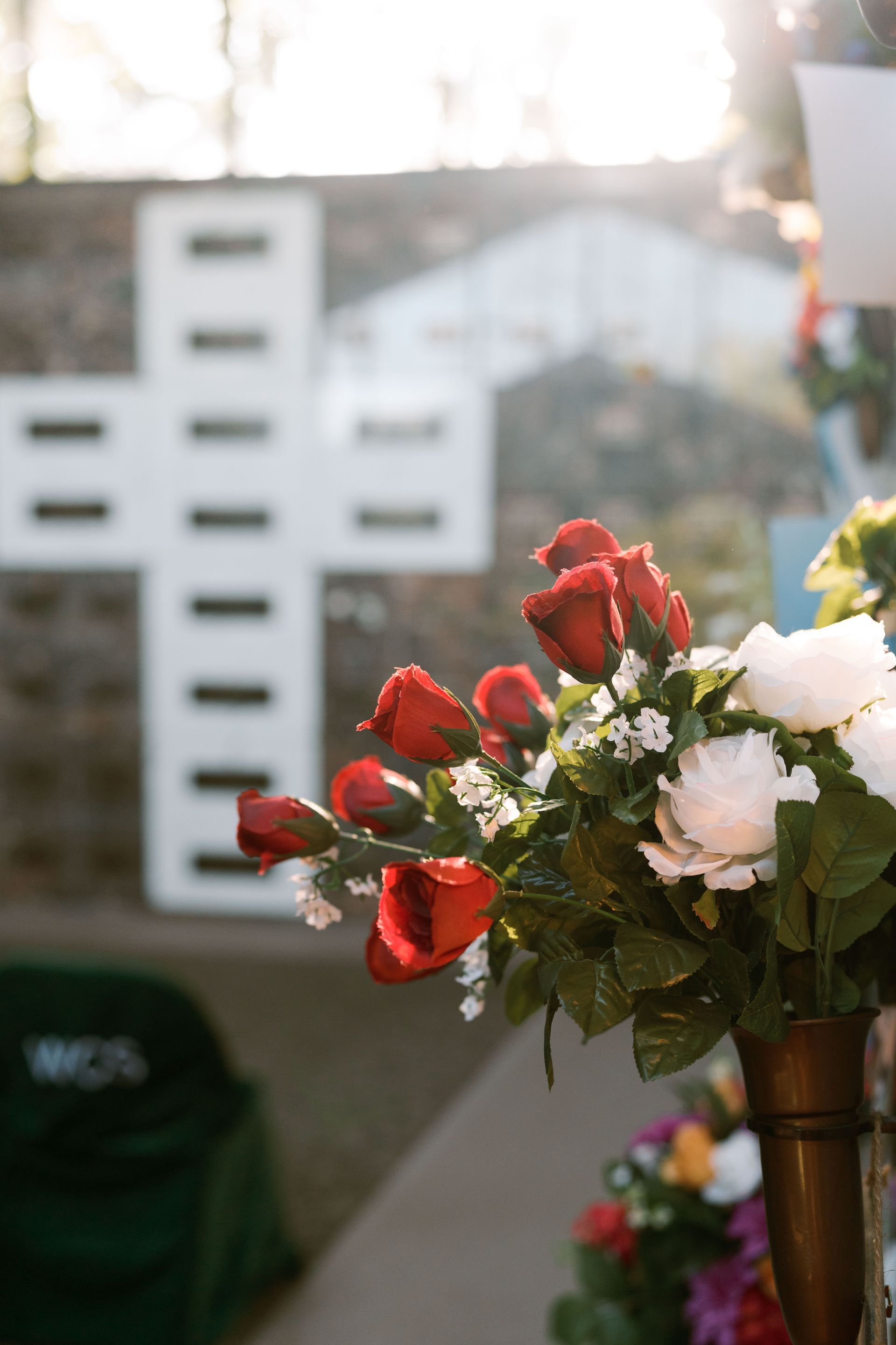 A vase of red and white roses in the foreground, with a large, white, grid-patterned cross in a blurred background.