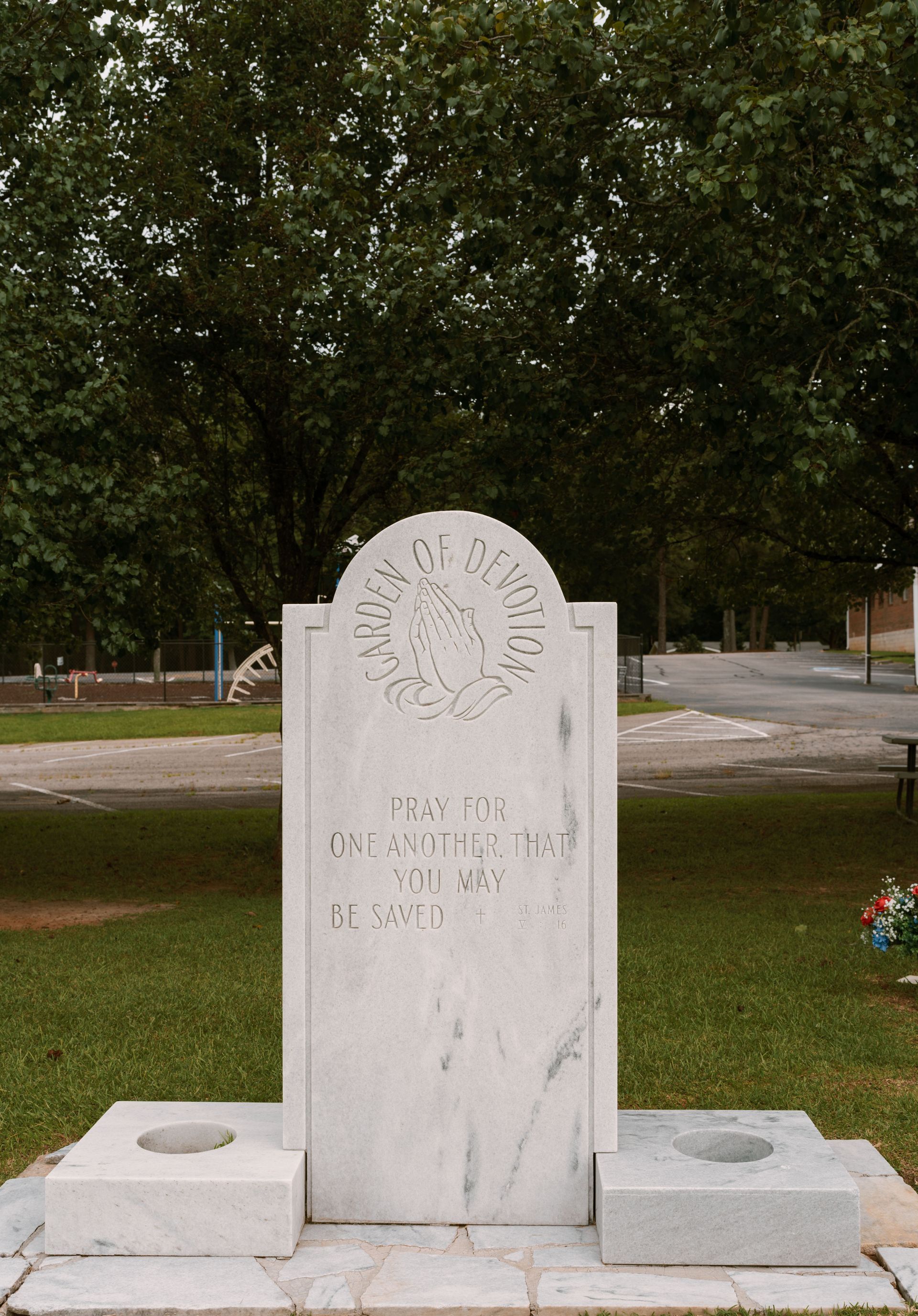 A white marble monument with the emblem of the Order of DeMolay, set in a grassy park area with trees in the background.