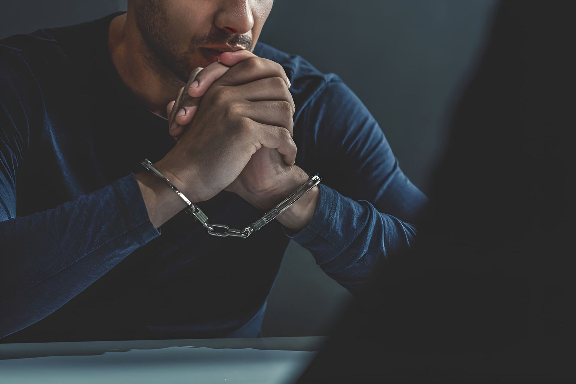 A Man In Handcuffs Is Sitting At A Table — Cairns Criminal Lawyers In Gordonvale, QLD