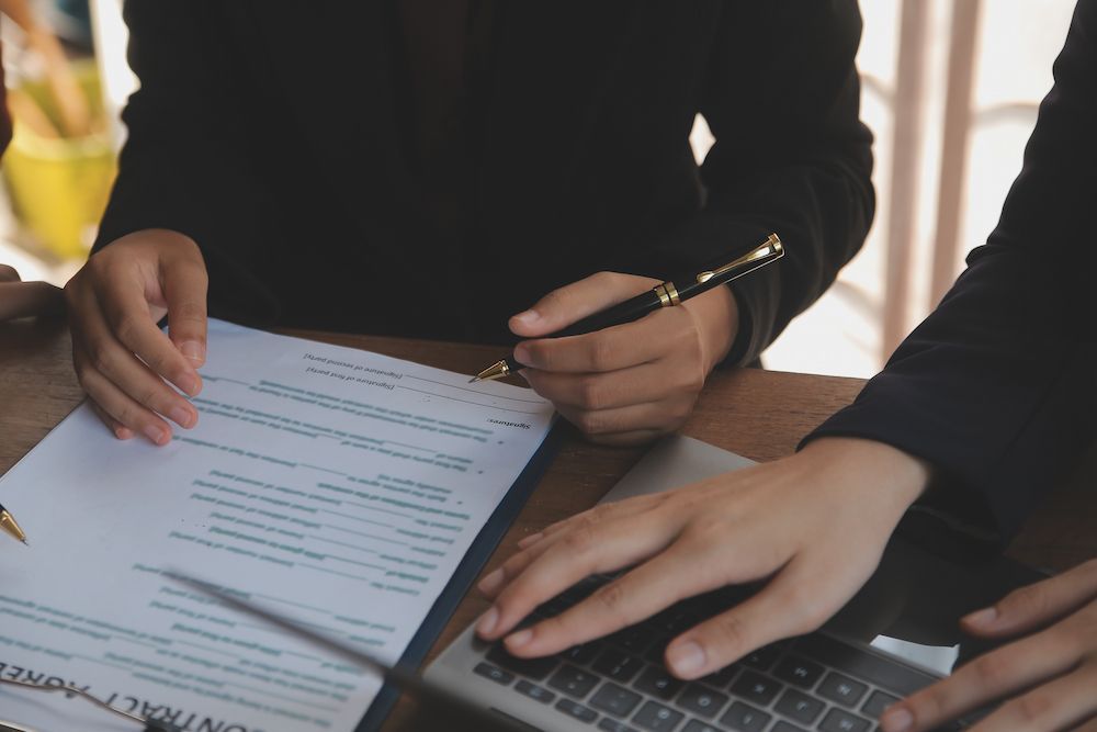 Two People Are Sitting at a Table Signing a Contract — Cairns Criminal Lawyers In Cairns City, QLD
