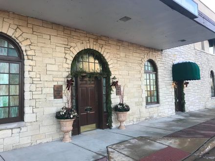 Exterior of a building with arched windows and doorway, light stone facade, and holiday decorations.