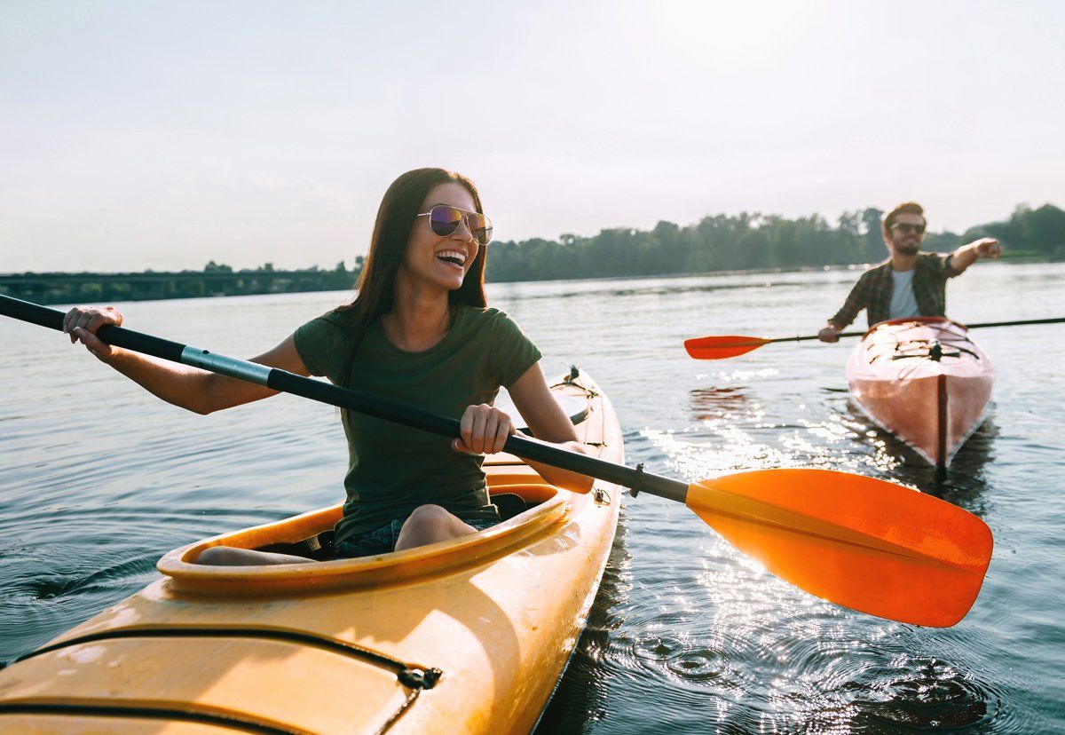 Two people kayaking on a lake, smiling and paddling in yellow and pink kayaks.
