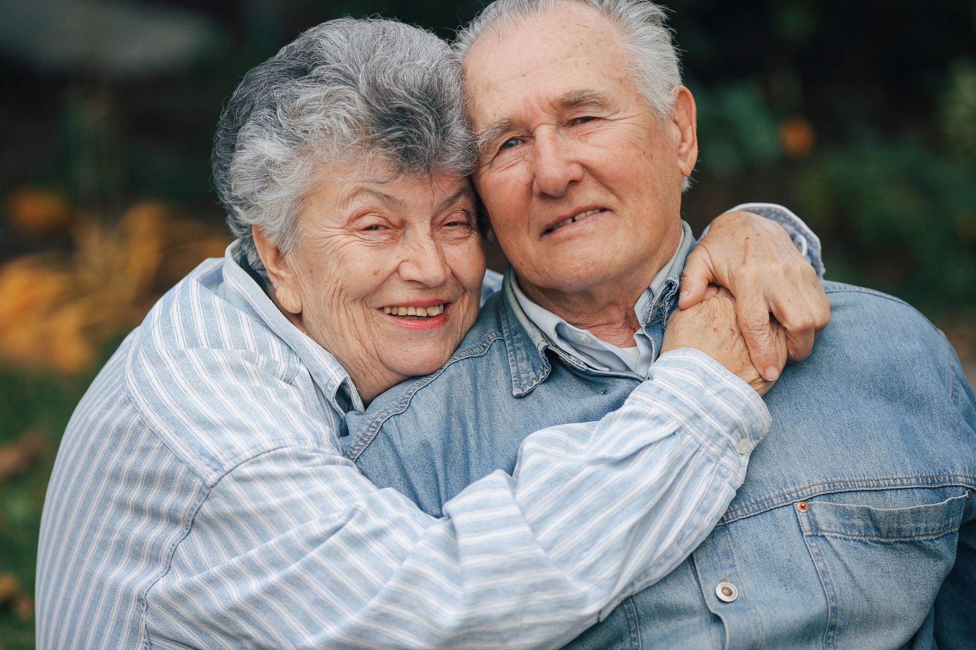 An elderly couple is hugging each other in a park.