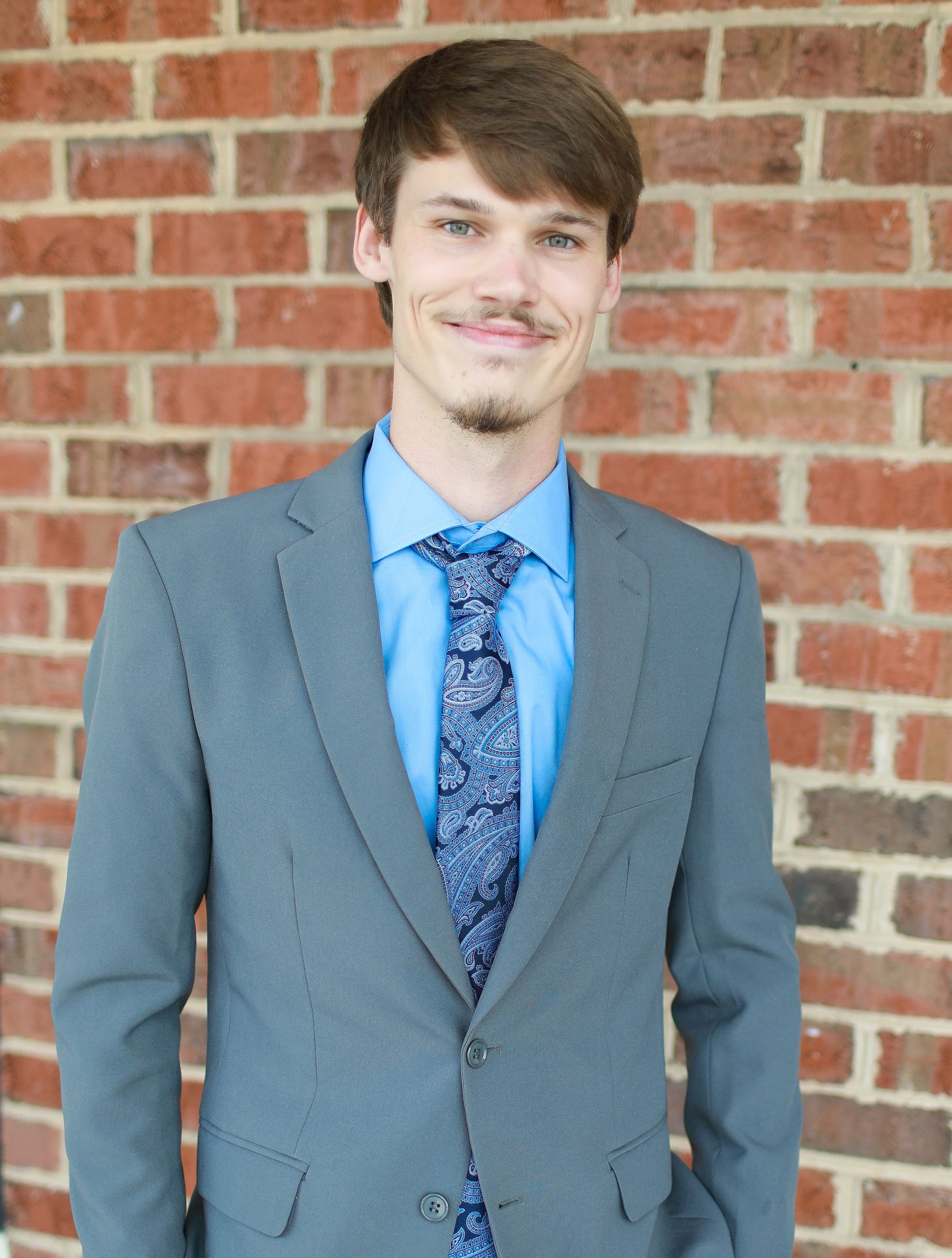 A young man is sitting in a chair in front of a brick wall.