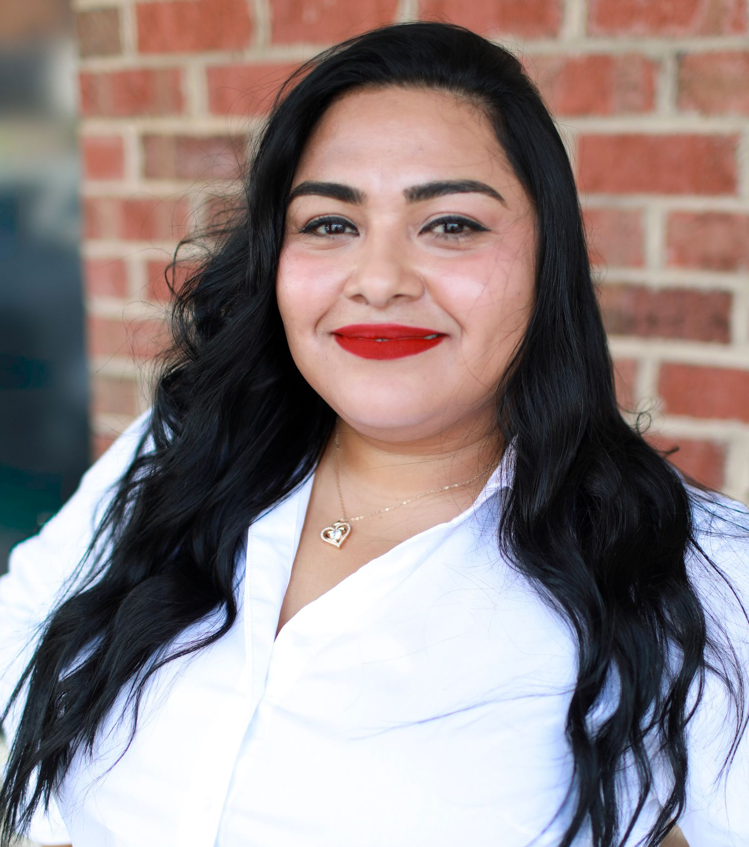 A woman is smiling in front of a brick wall.