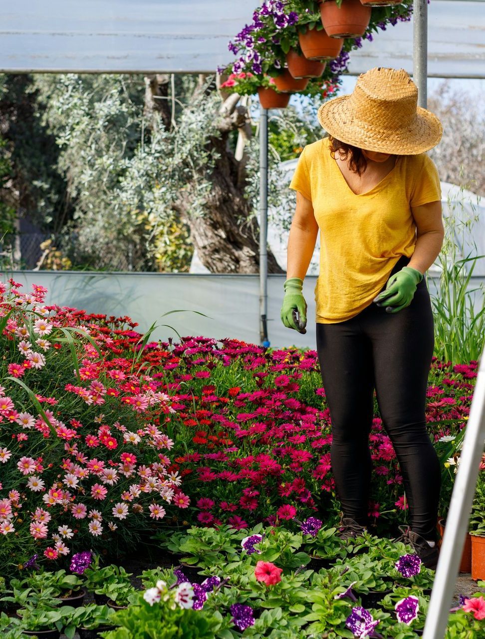 A woman is working in a greenhouse surrounded by flowers.