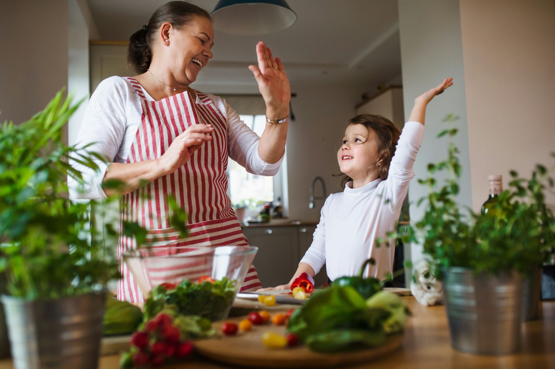 A woman and a child are dancing in the kitchen while preparing food.