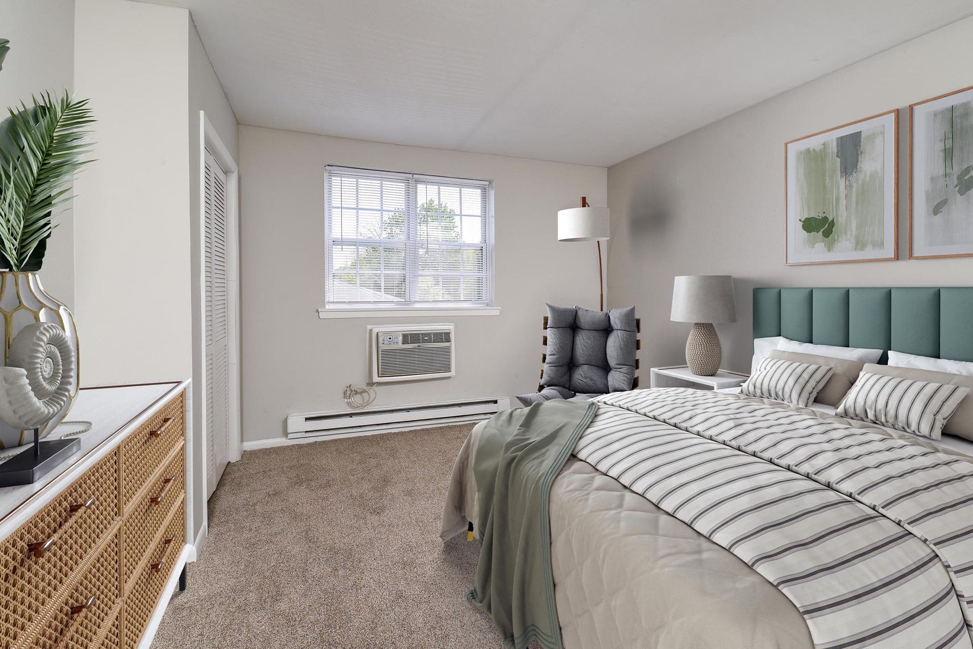 Furnished apartment bedroom with a bed, dresser, chair, and window air conditioner.