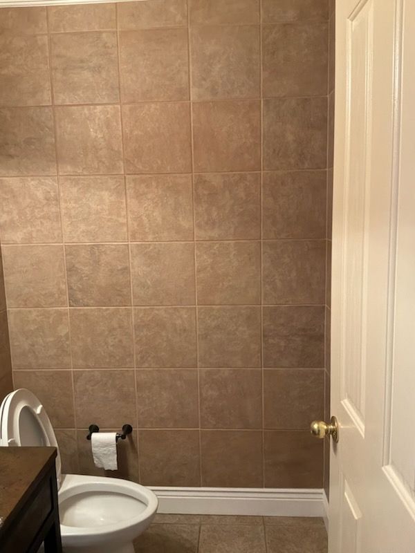 Small bathroom with brown tiled wall, white toilet, and white door.