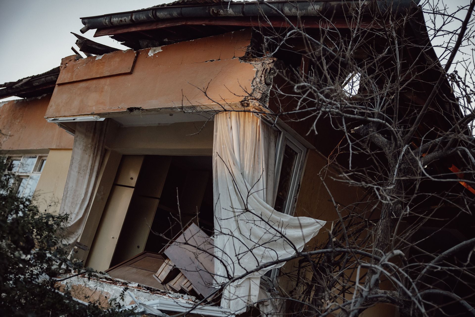 Collapsed house with cracked walls, broken roof, and debris tangled in nearby branches