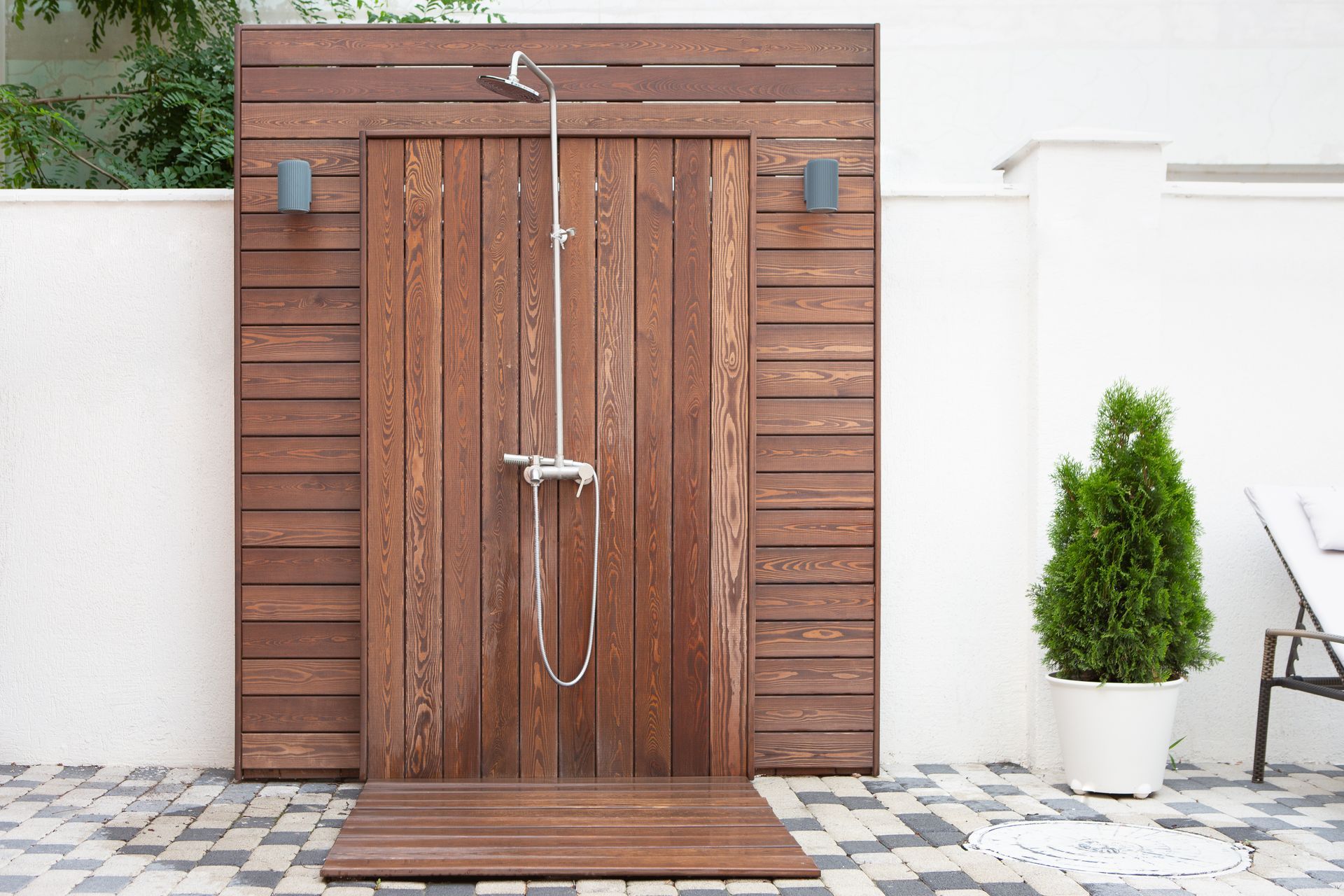 Wooden outdoor shower stall with metal fixtures against a white wall