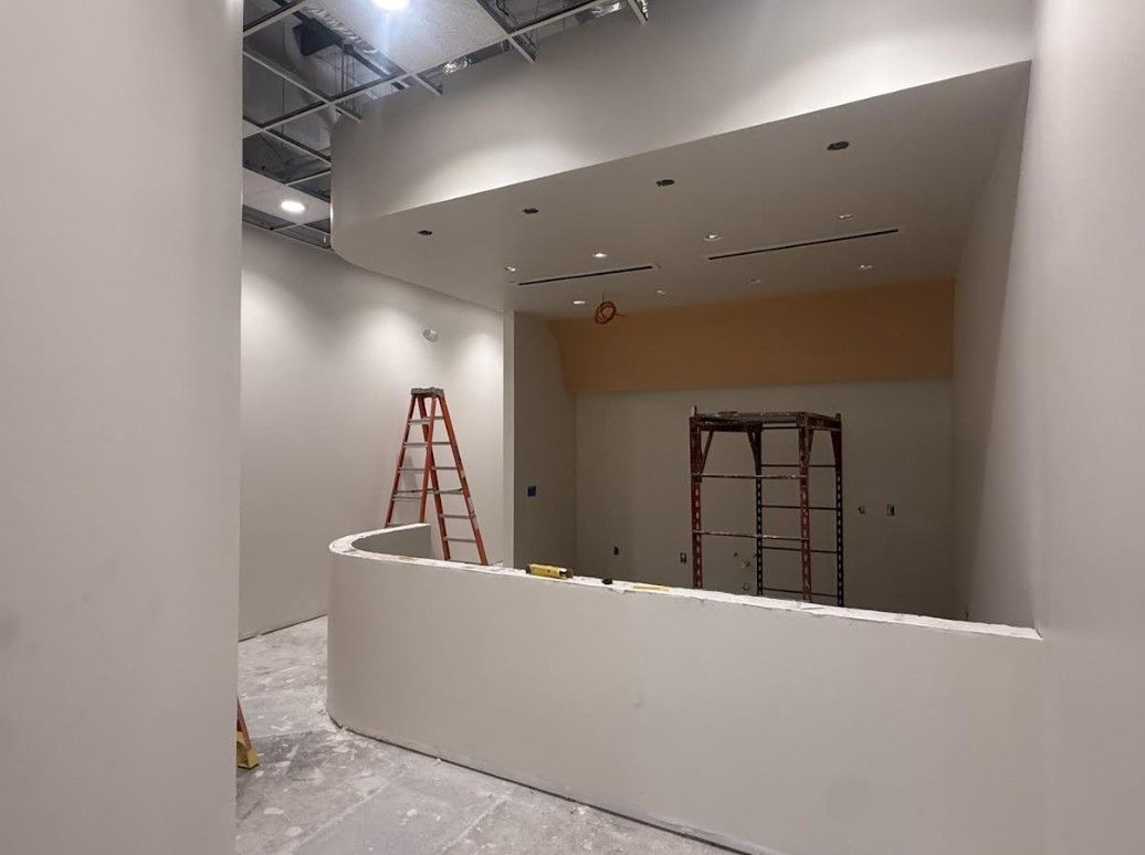 Interior renovation site with white curved wall, red ladder, and scaffolding under construction lighting