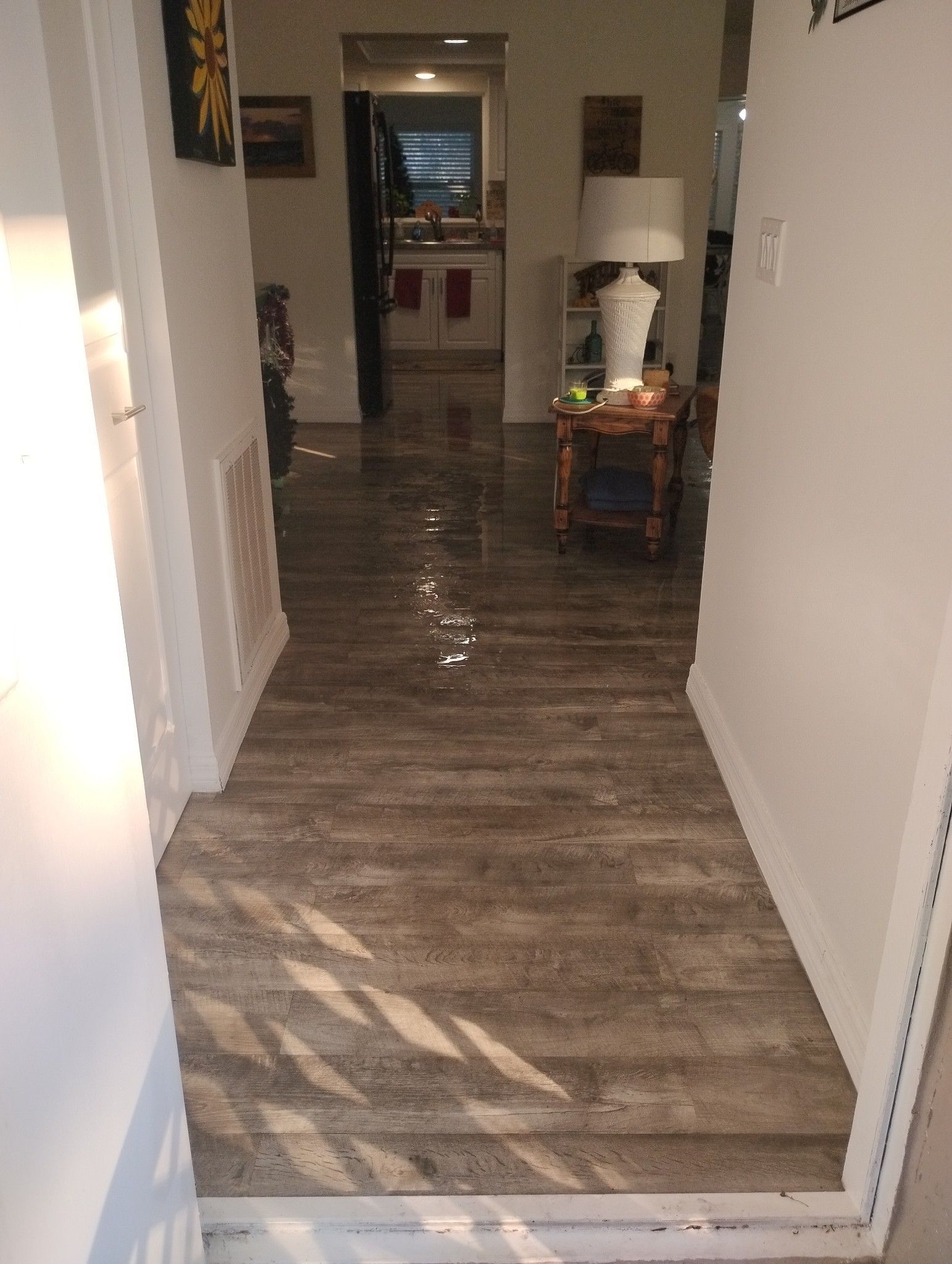 A hallway with a wooden floor and a lamp on a table.