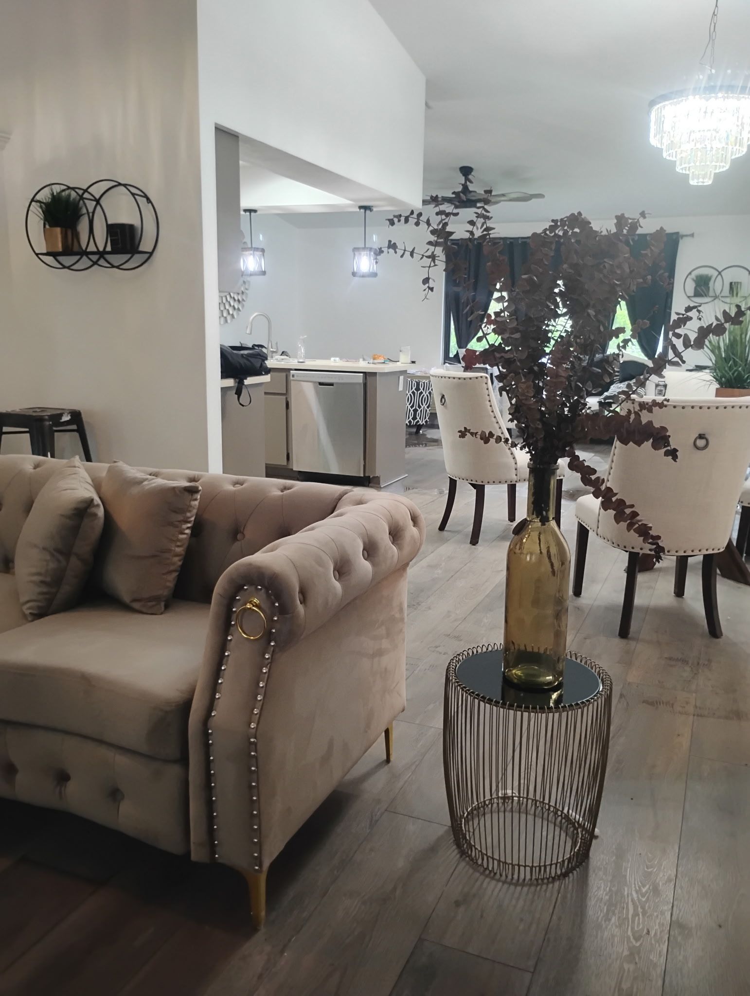 Living room with tan sofa, gold-studded details, vase of branches on a side table, dining area in background.