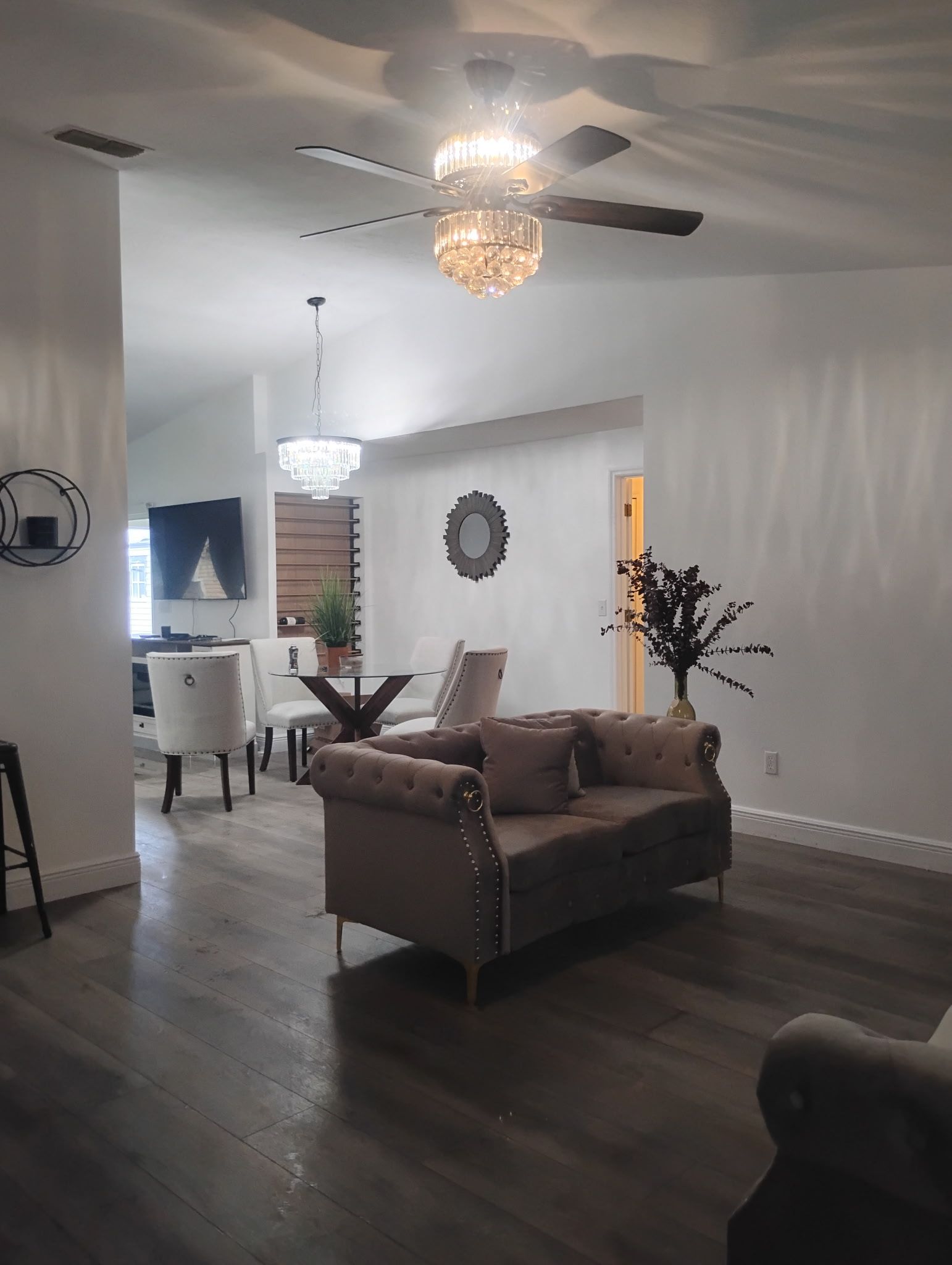 Living room with dark wood floors, white walls, and a decorative crystal chandelier.