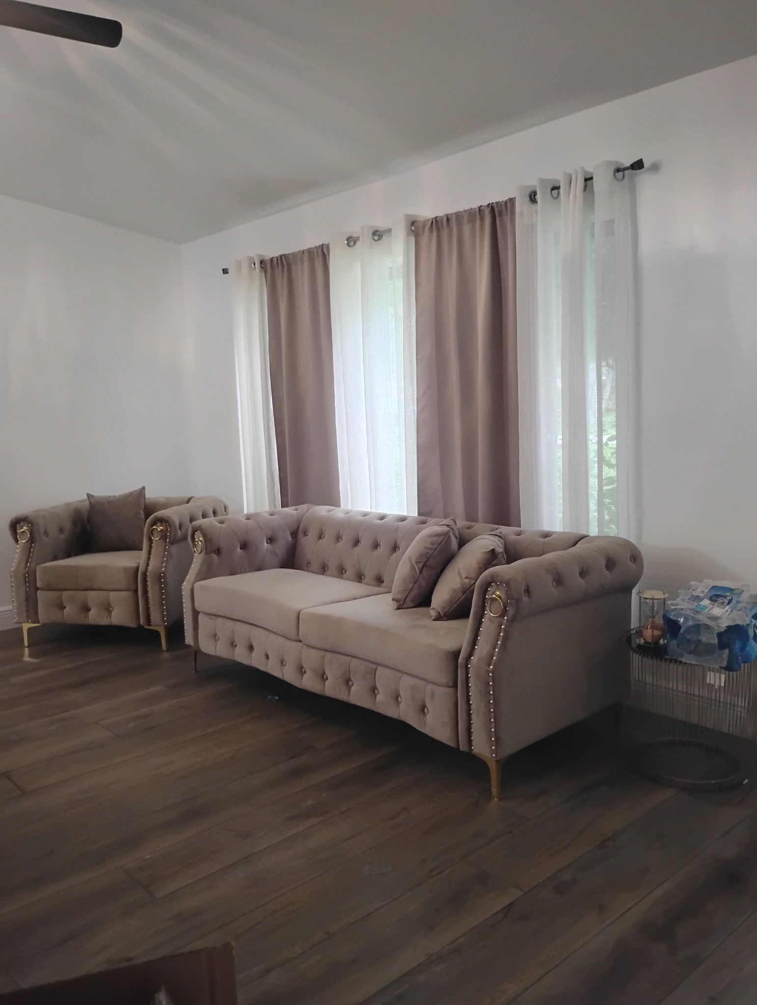Living room with a tufted sofa, armchair, curtains, and wood flooring.