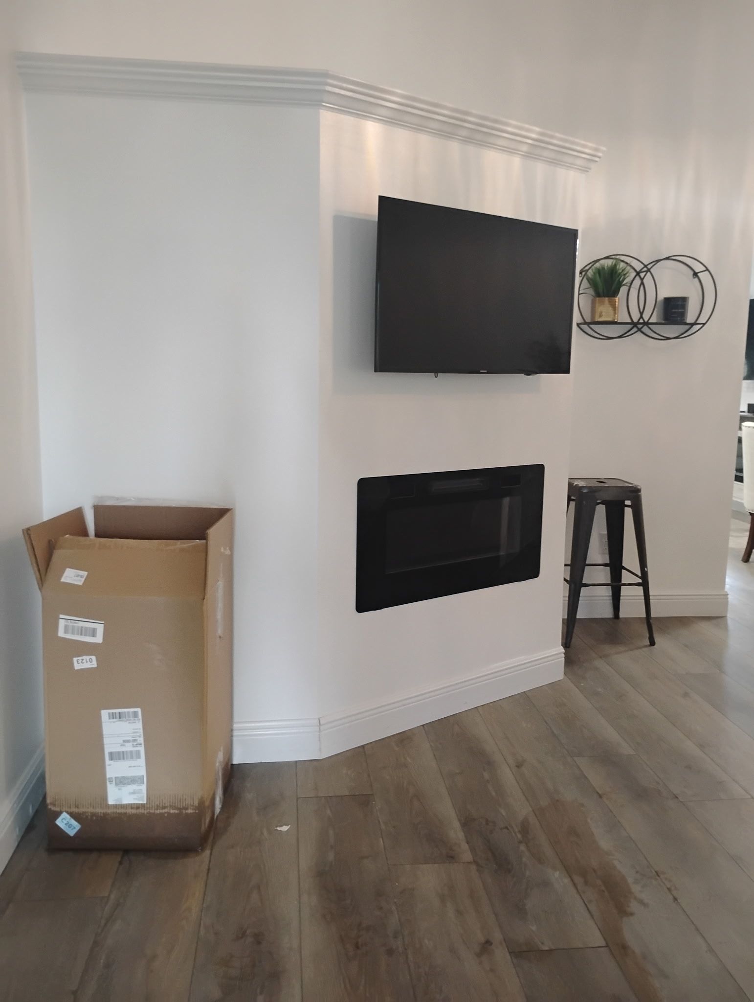 A modern living room with a TV mounted above a black fireplace. A cardboard box sits nearby.
