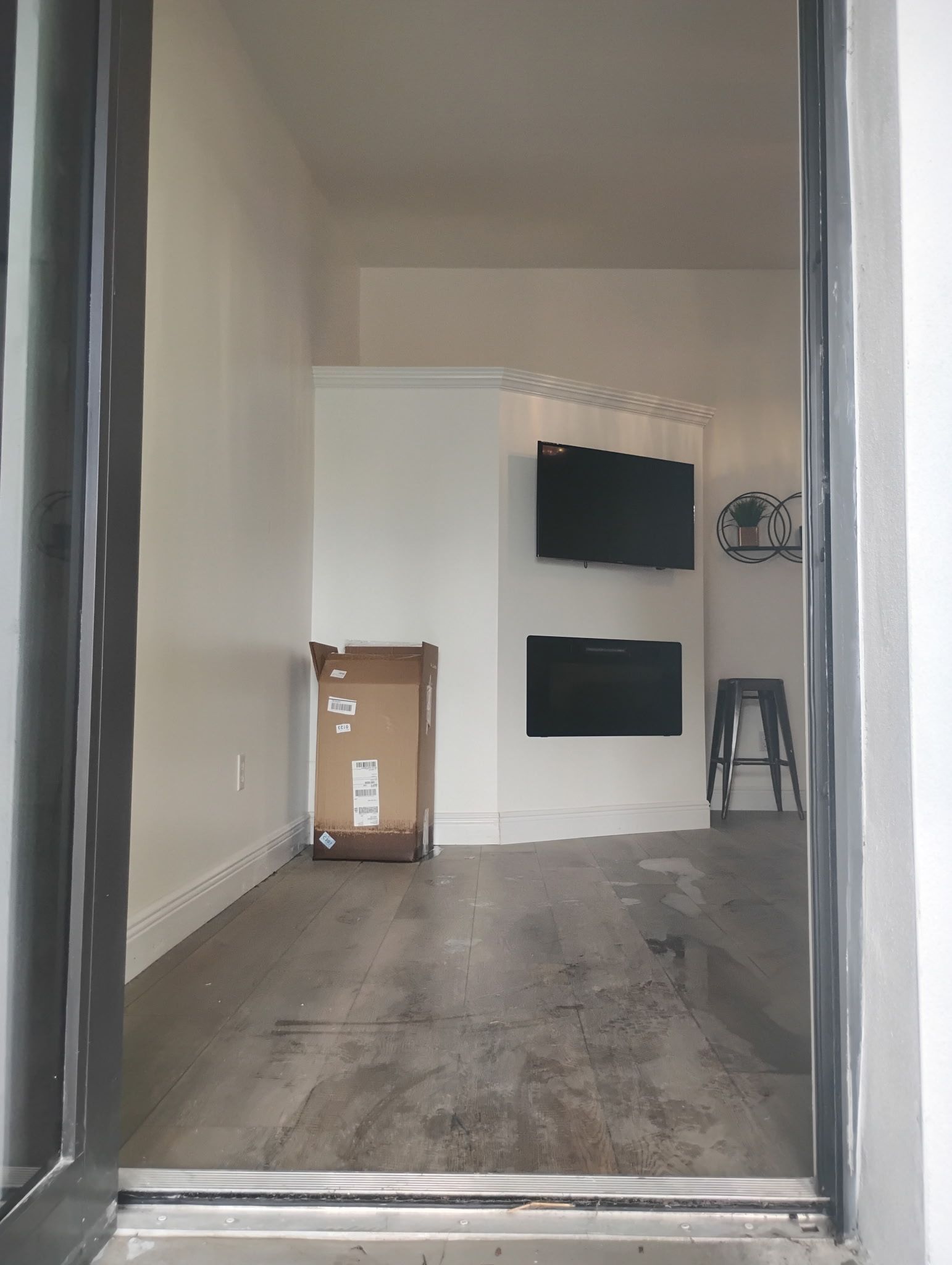 Interior room view; white walls, fireplace with two black screens, cardboard box on floor, and a metal chair.