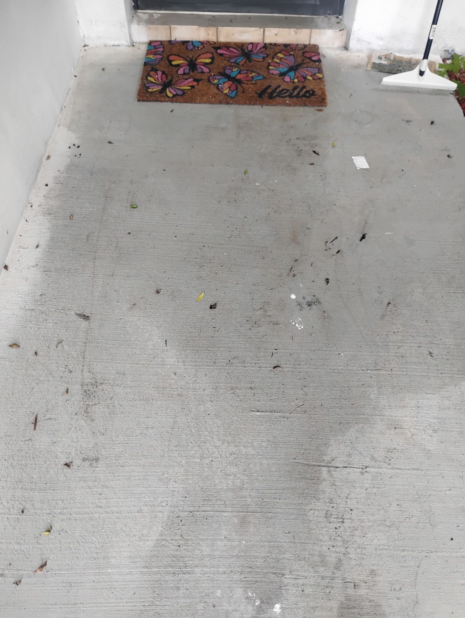 Concrete porch with a doormat in front of a door. Debris is scattered on the ground.