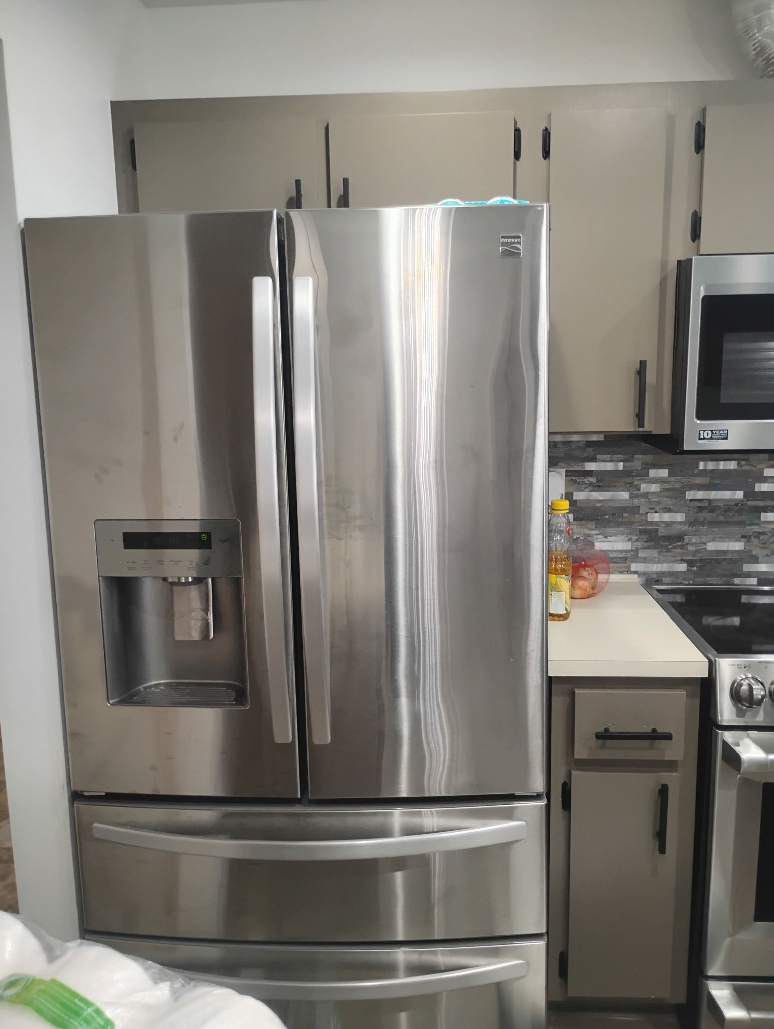 Stainless steel refrigerator in kitchen with gray cabinets and backsplash.