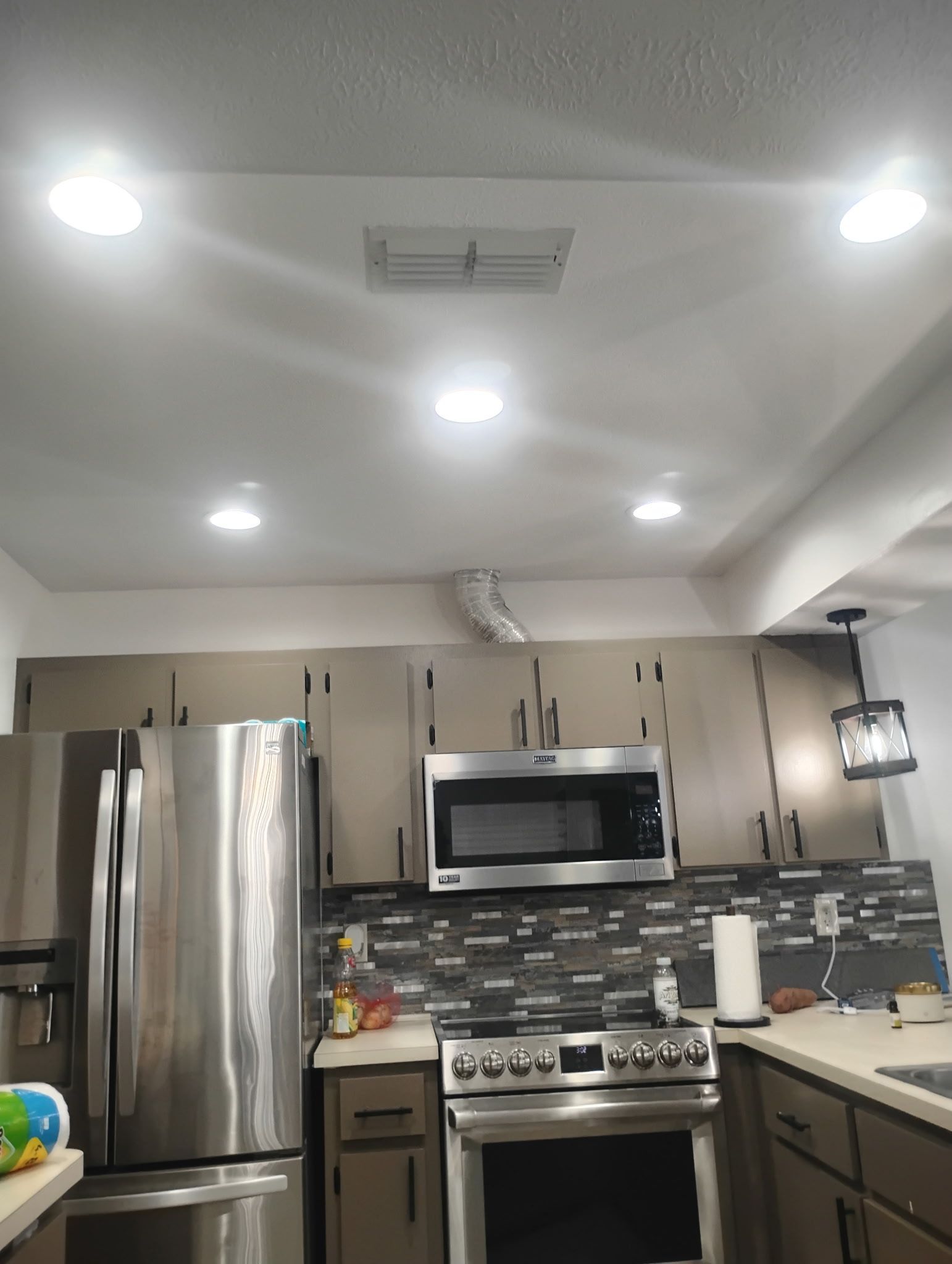 Kitchen with stainless steel appliances, neutral cabinets, gray backsplash, and recessed ceiling lights.