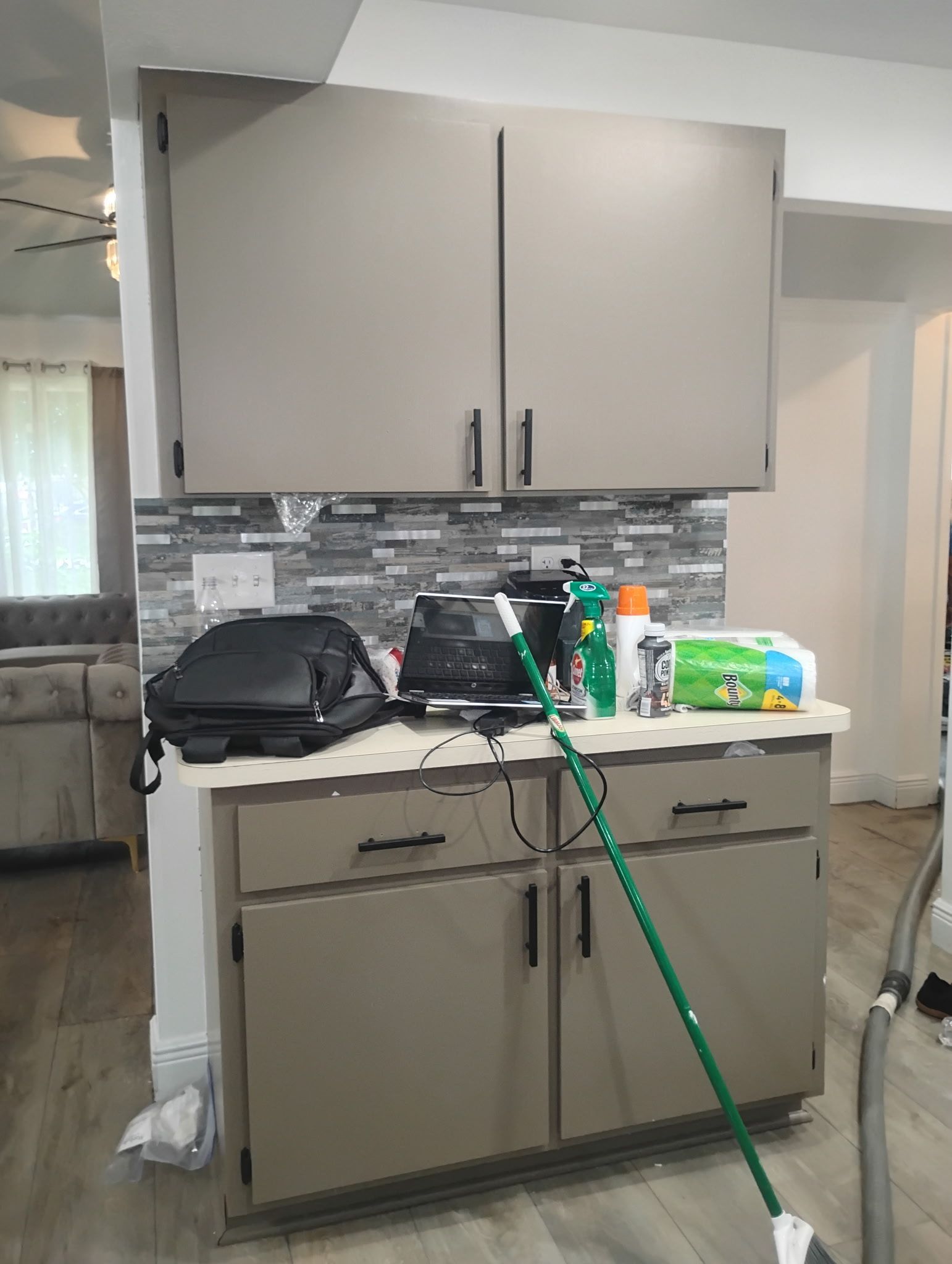 Gray kitchen cabinets with a tiled backsplash. Countertop with appliances and cleaning supplies.