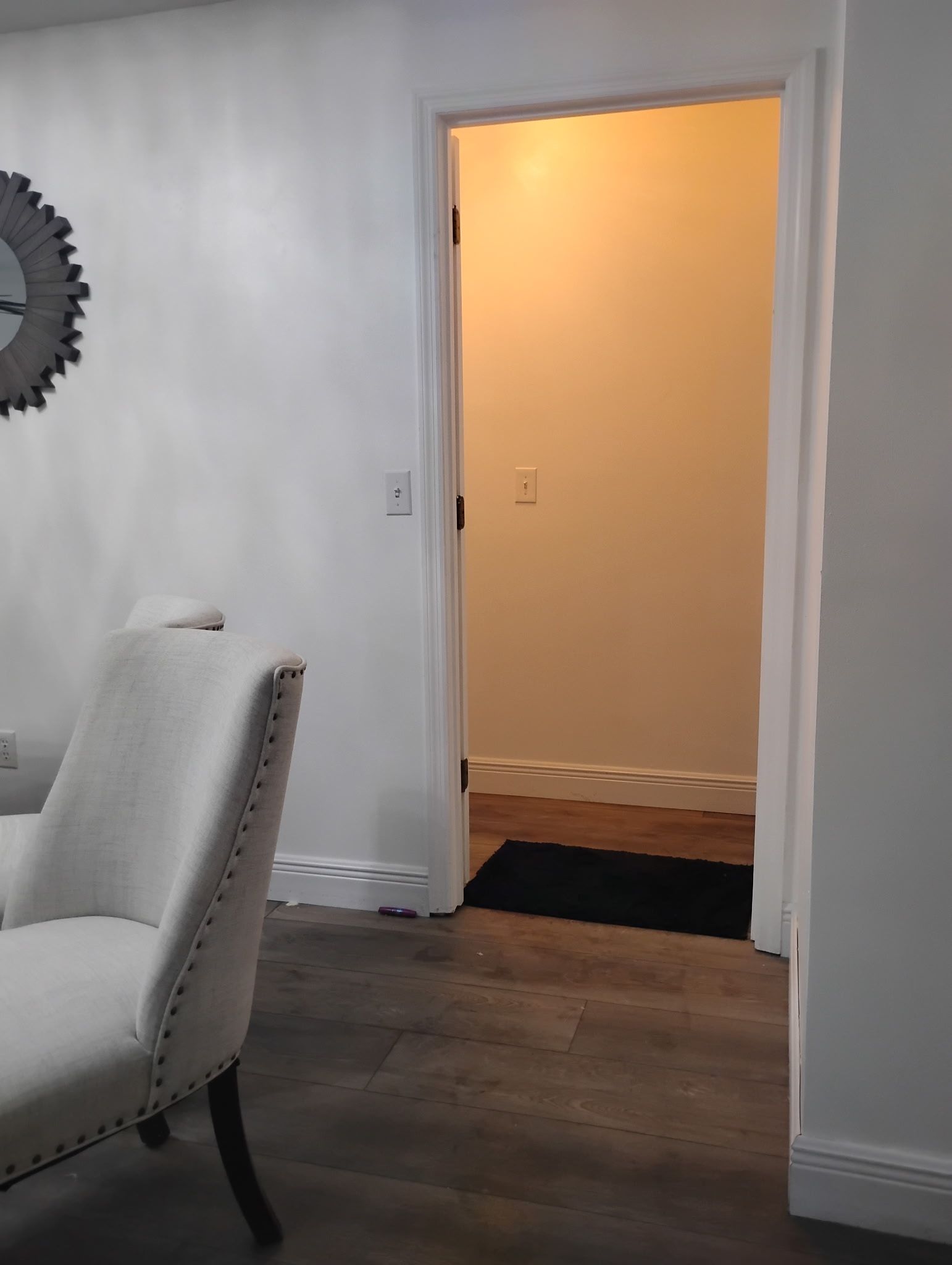 White chair, doorway, and mirror on a white wall. Dark floor.