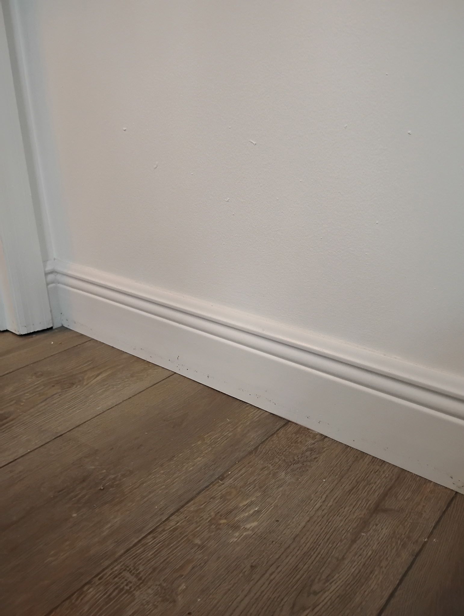 White baseboard molding along white wall and wood-look floor.
