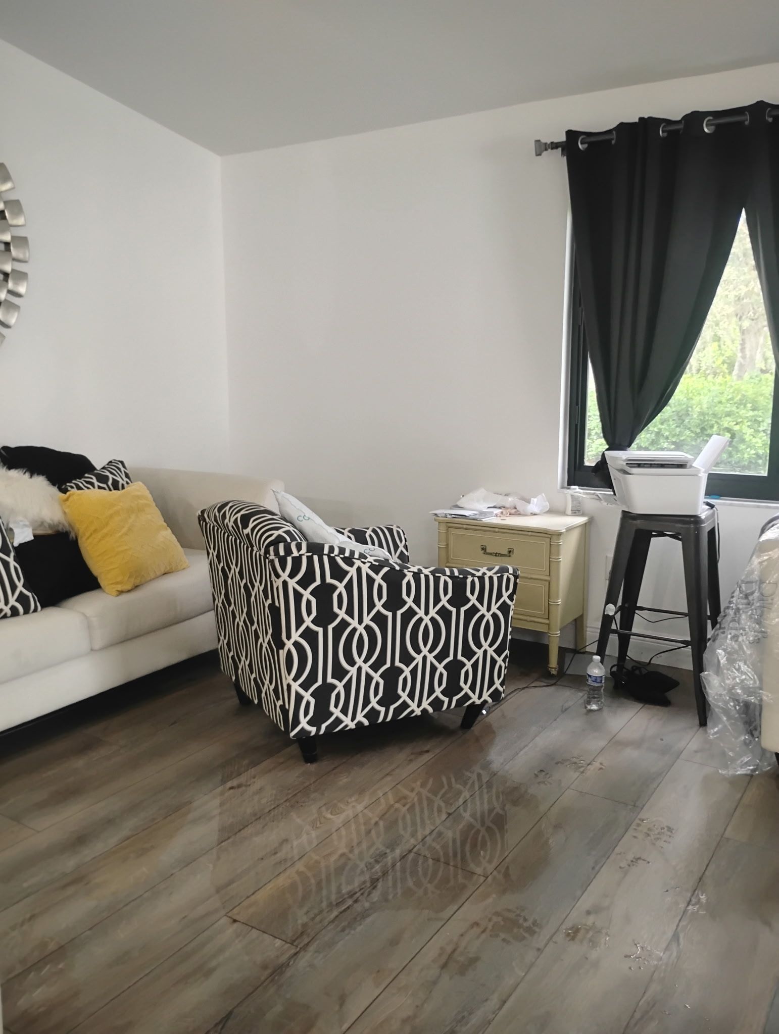 Living room with white walls, patterned armchair, white couch, black curtains, and wooden floor.