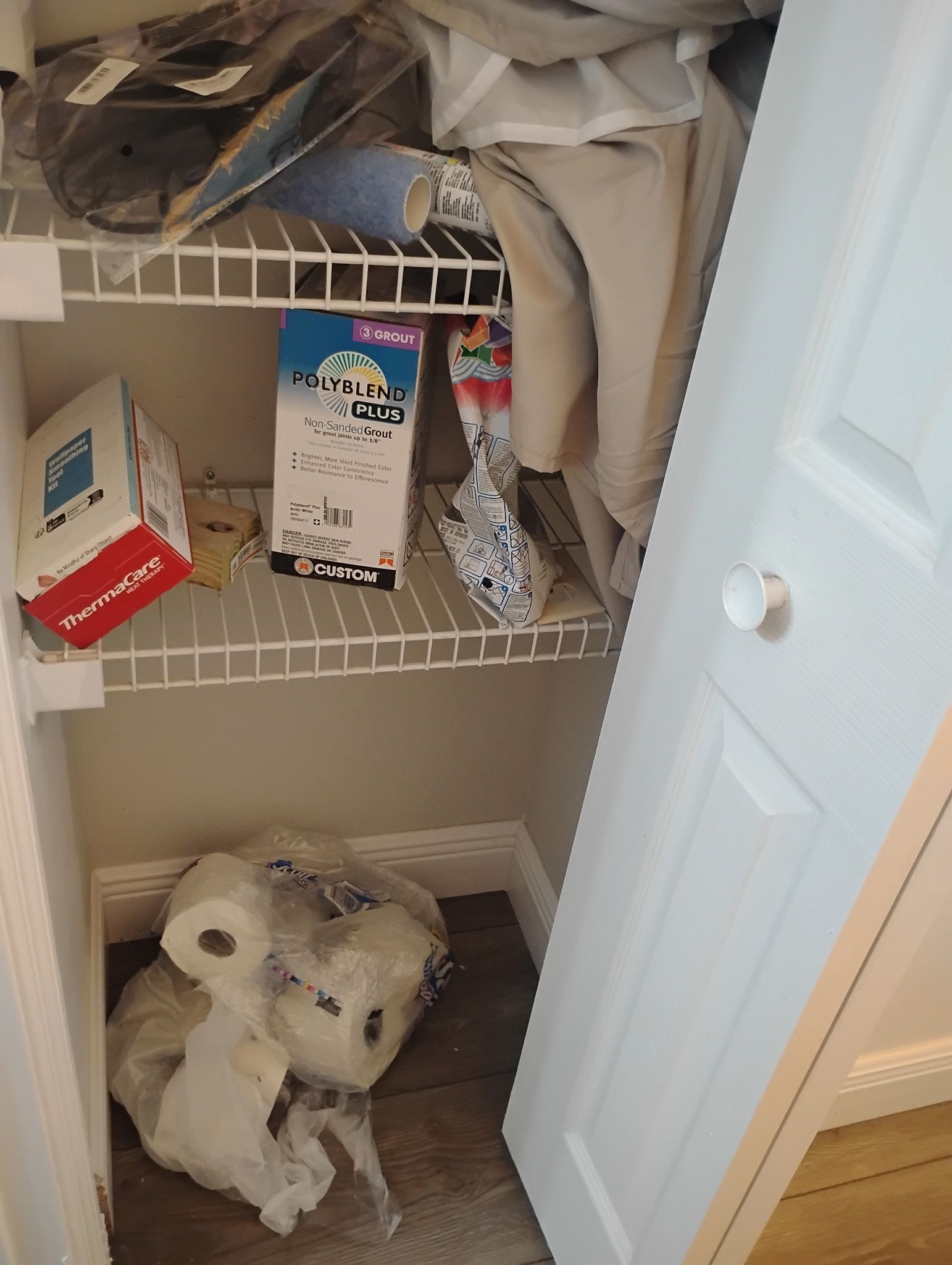 A cluttered storage closet with shelves. Toilet paper and other items are stored.