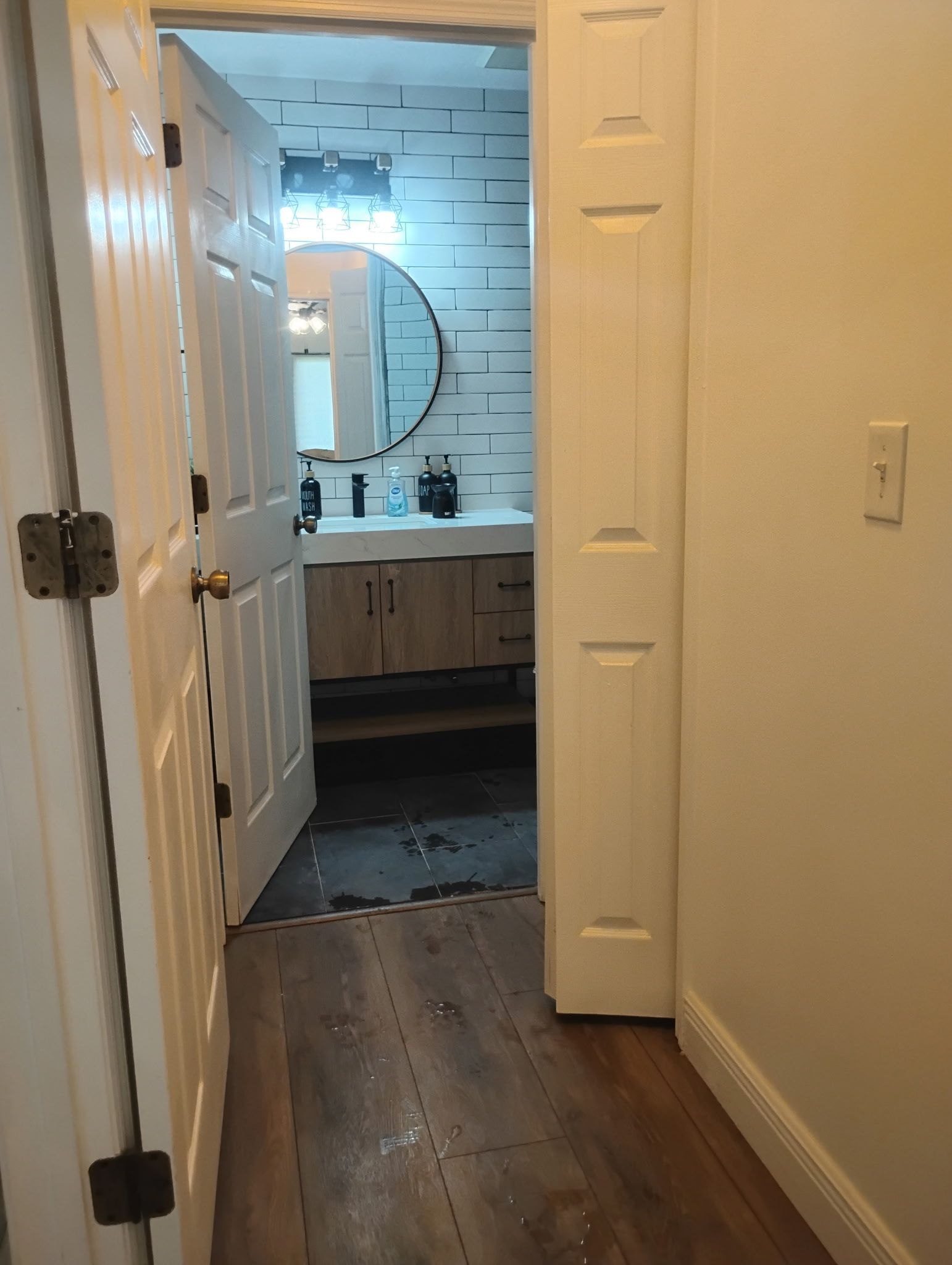 A hallway with a partially open door to a bathroom; white trim, wood-look floor.