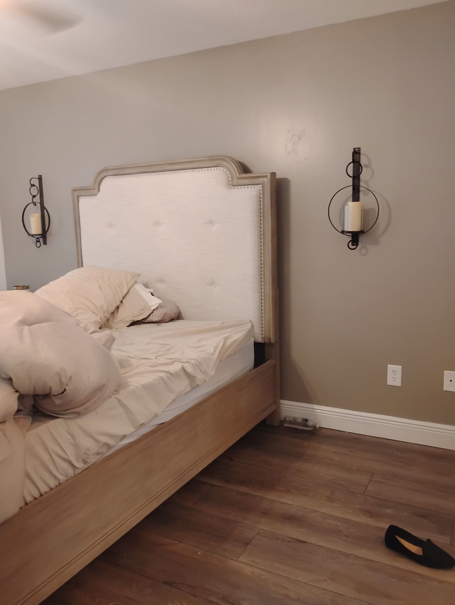 Bedroom with bed, headboard, wall sconces, and hardwood floor.