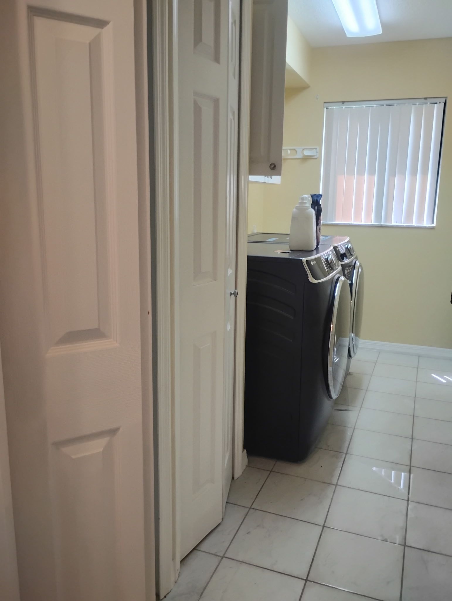 Laundry room with washer, dryer, white tile floor, and a closed white door.