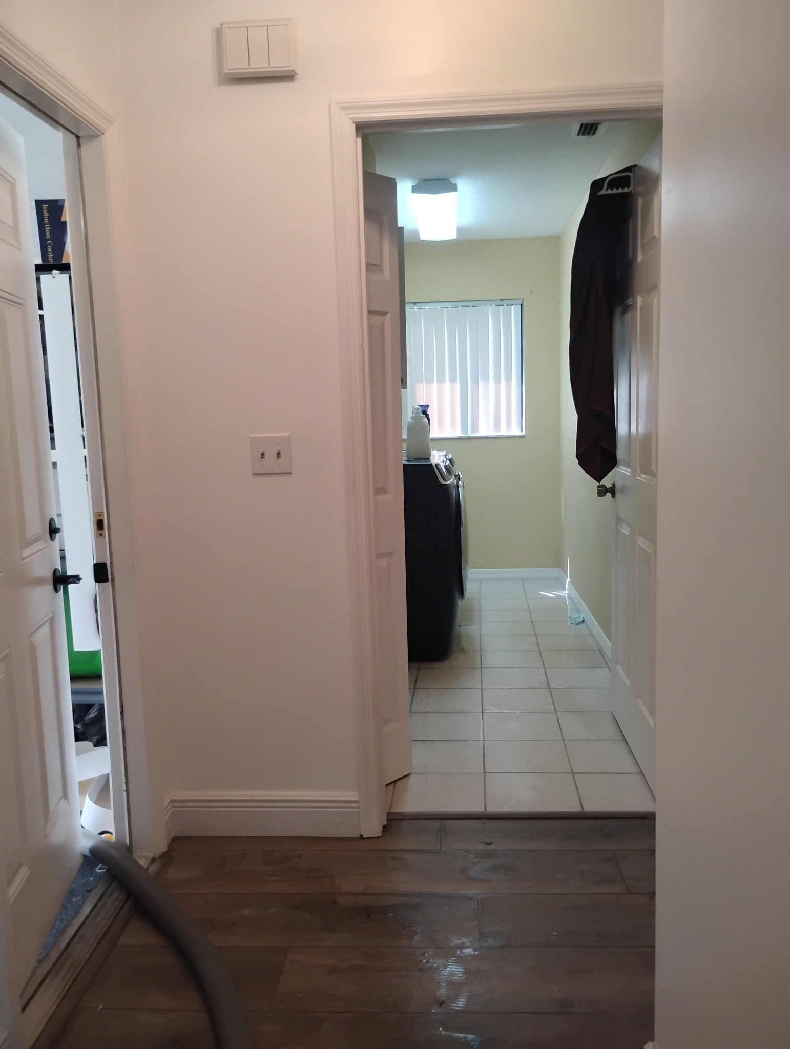 Hallway with open doors, wood and tile floors, and a hanging coat.