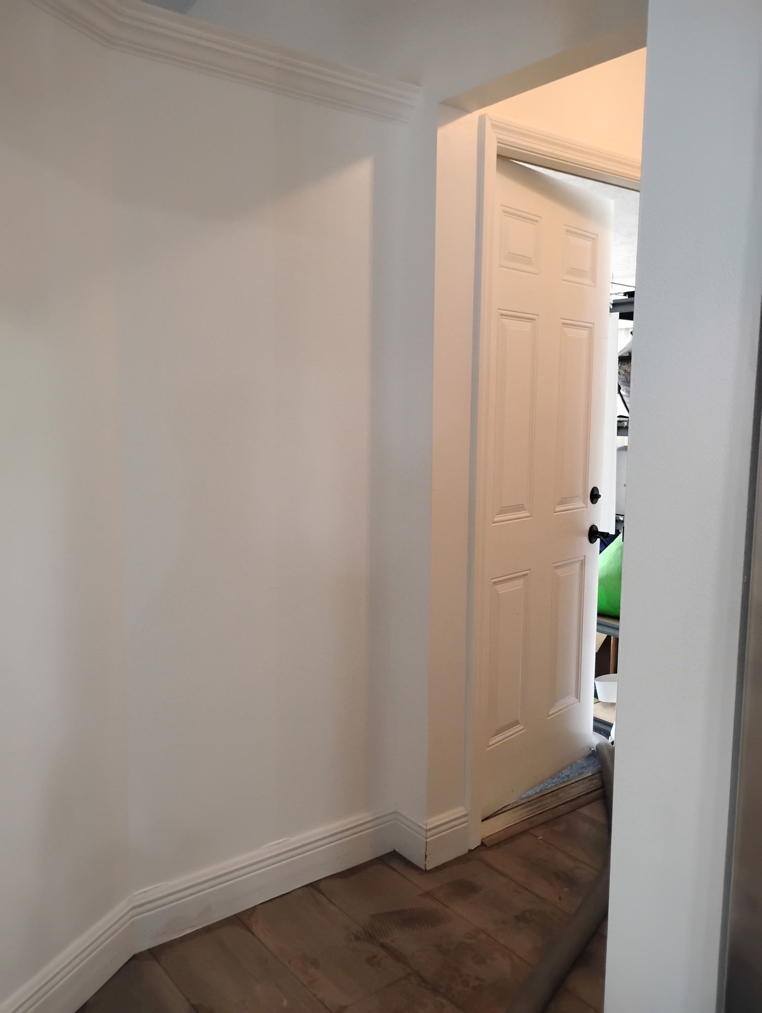 White hallway with open door. Door frame and molding are white, door slightly ajar.